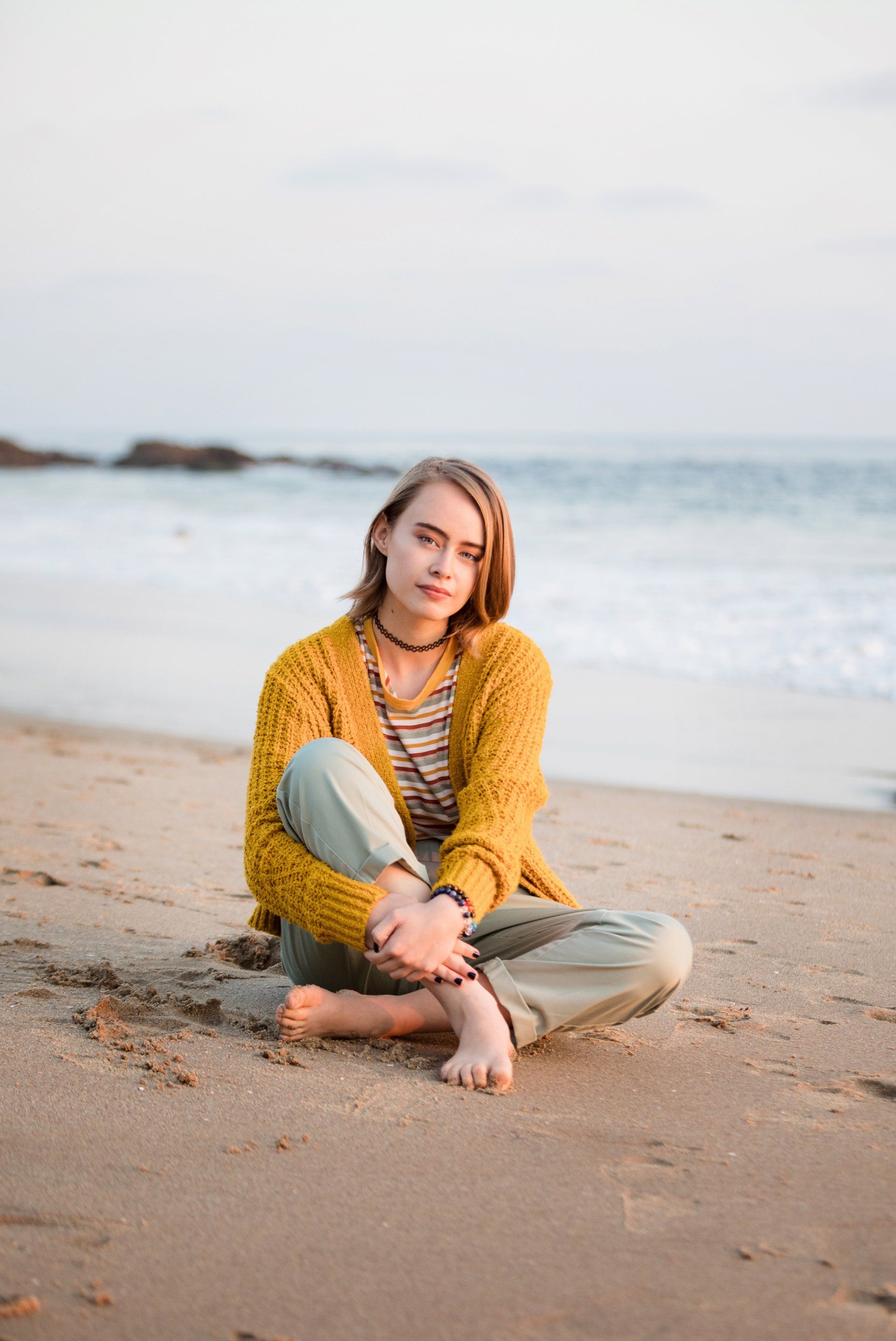 A woman is sitting on the beach with her legs crossed.