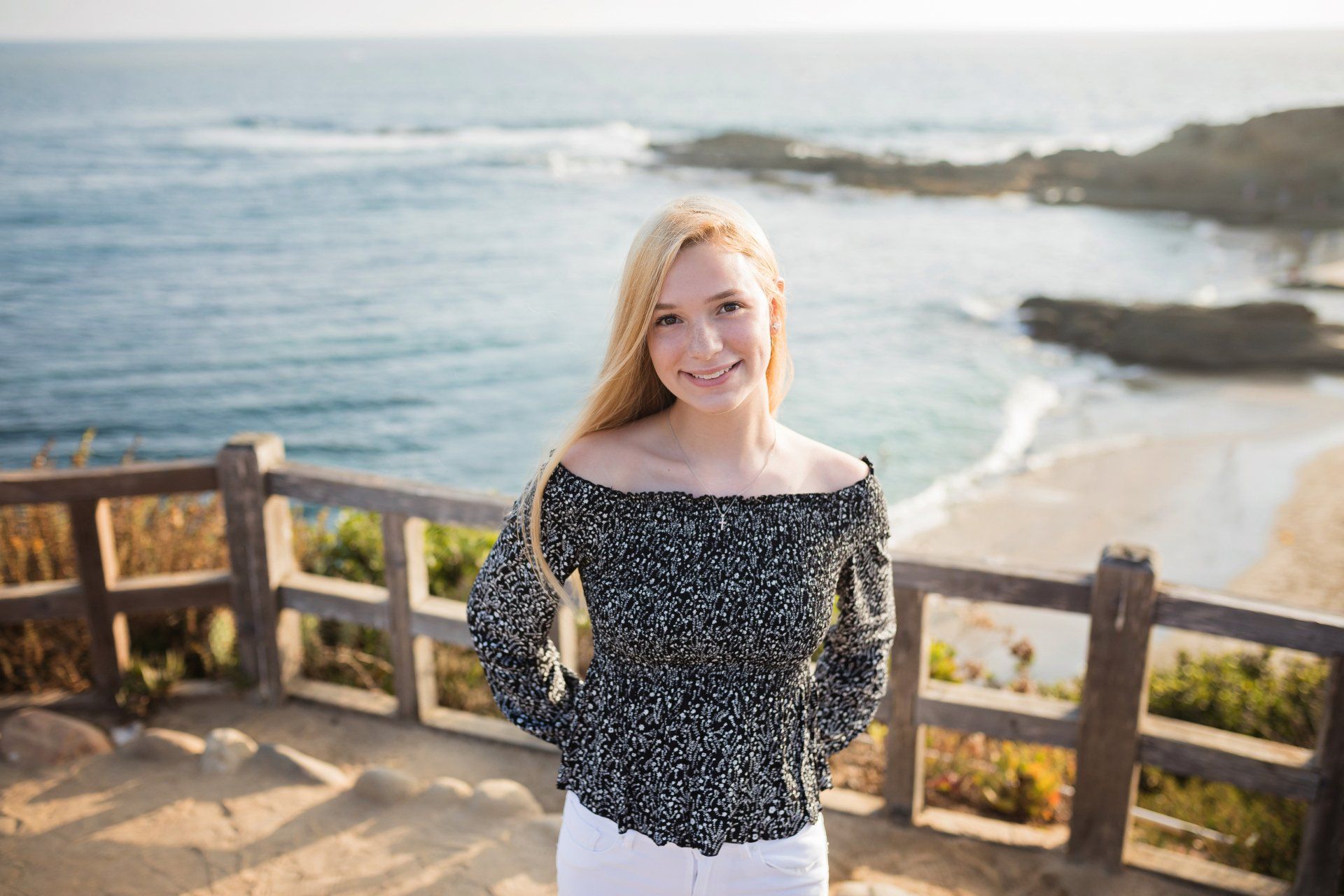 A young woman is standing on a cliff overlooking the ocean.
