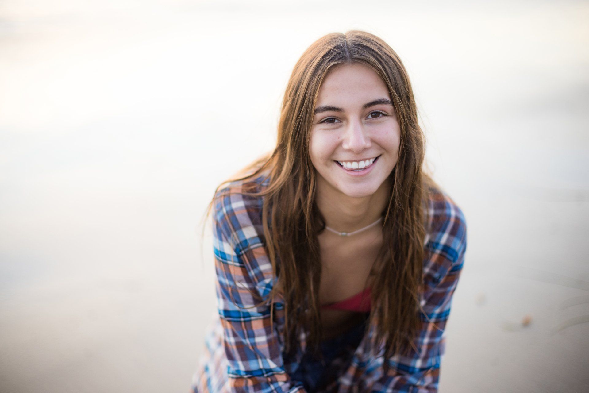 A young woman in a plaid shirt is smiling on the beach.