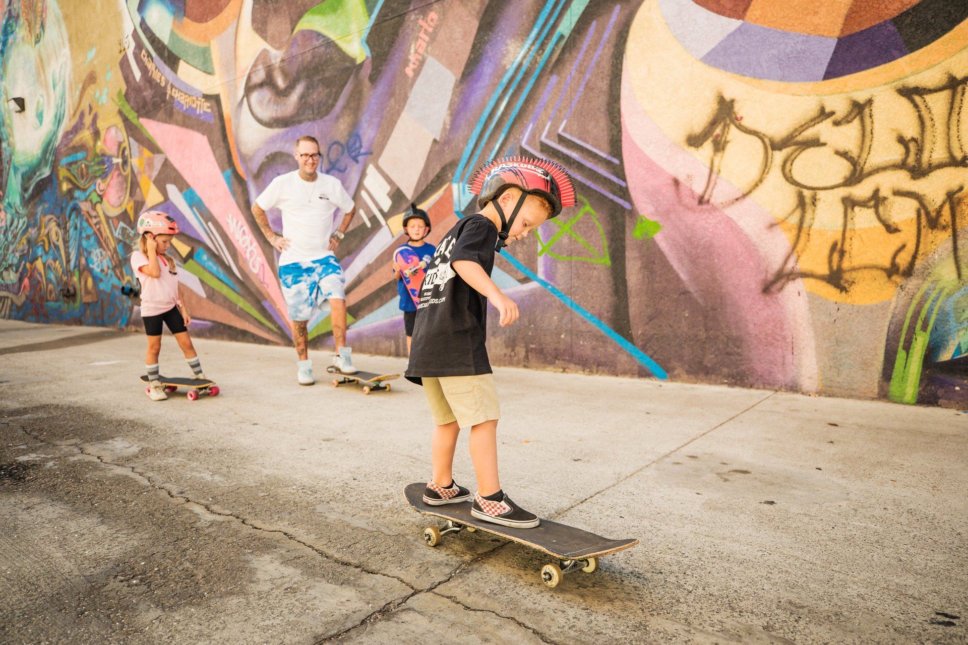 A group of people are riding skateboards in front of a graffiti wall.