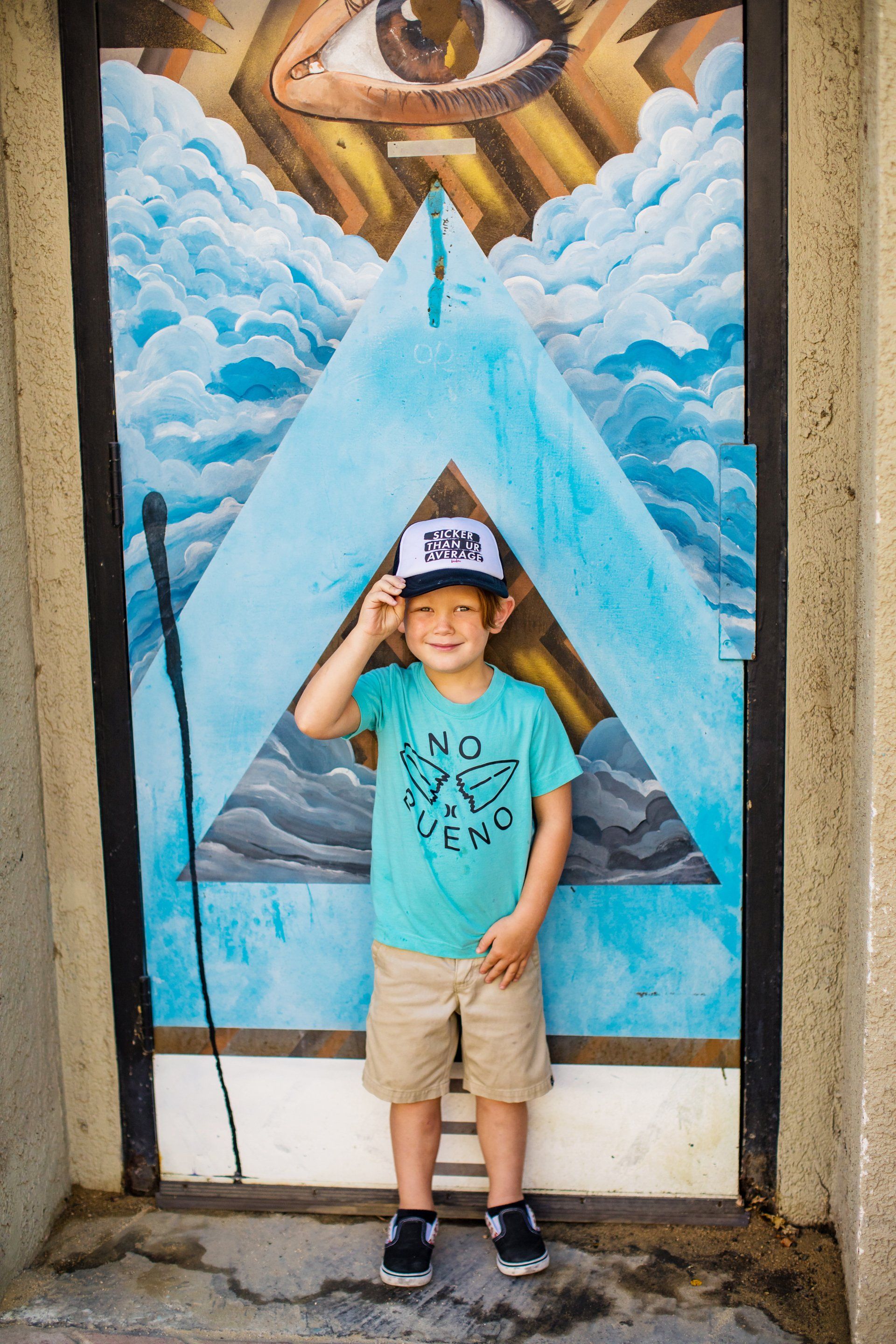A young boy wearing a hat is standing in front of a mural.