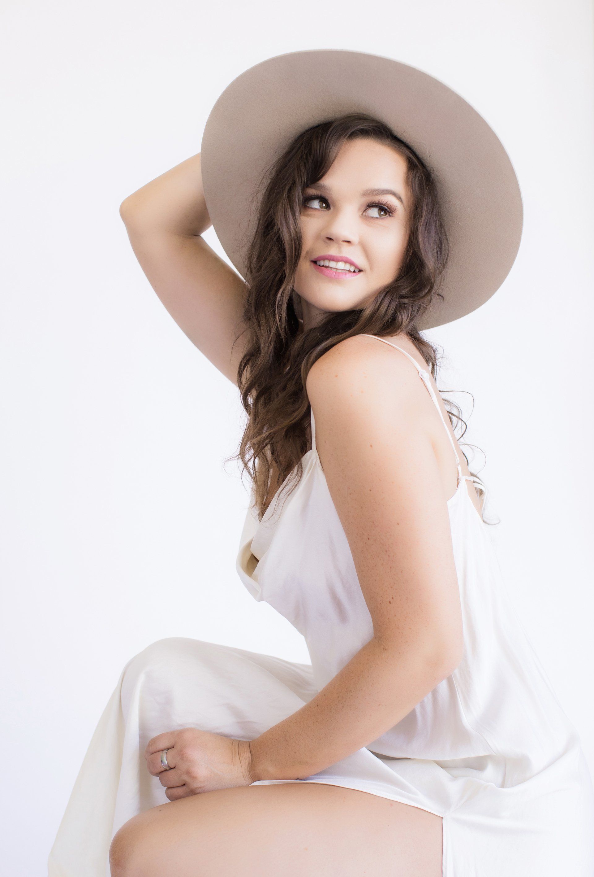 A woman in a white dress and hat is sitting on a stool.