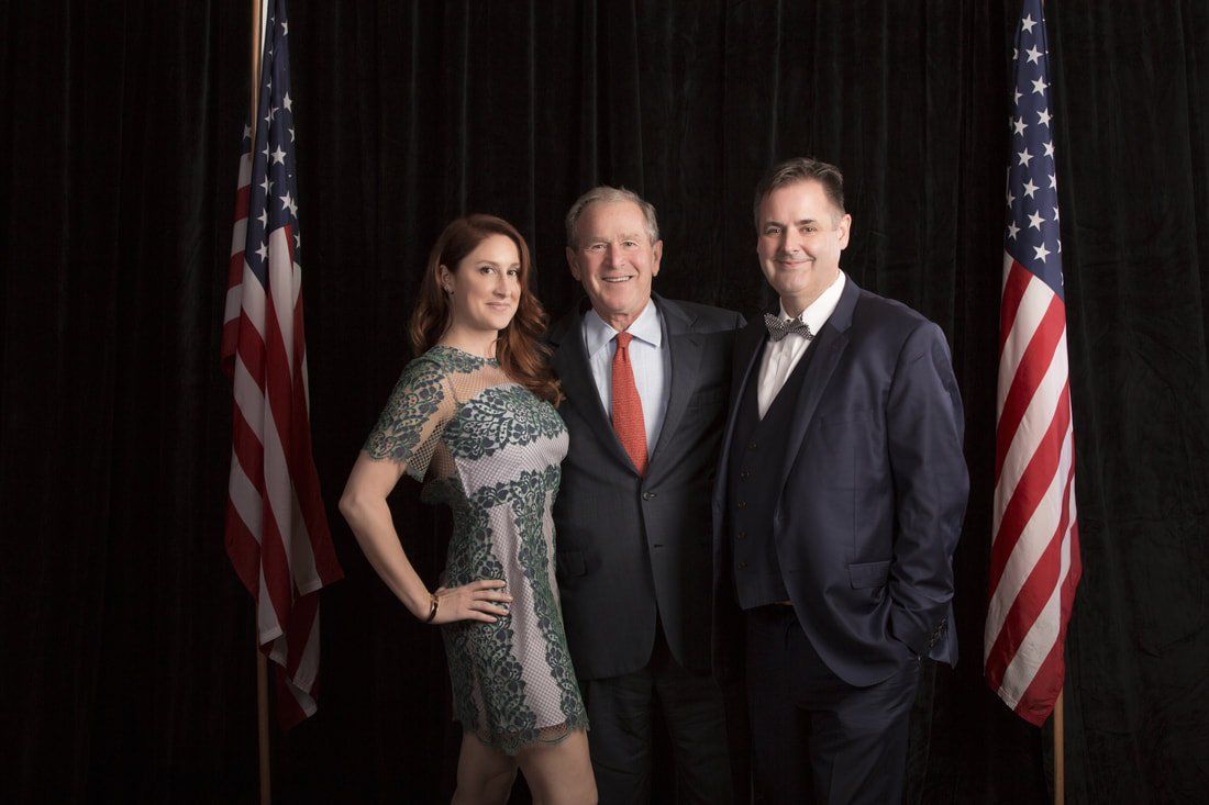 Three people are posing for a picture in front of american flags.