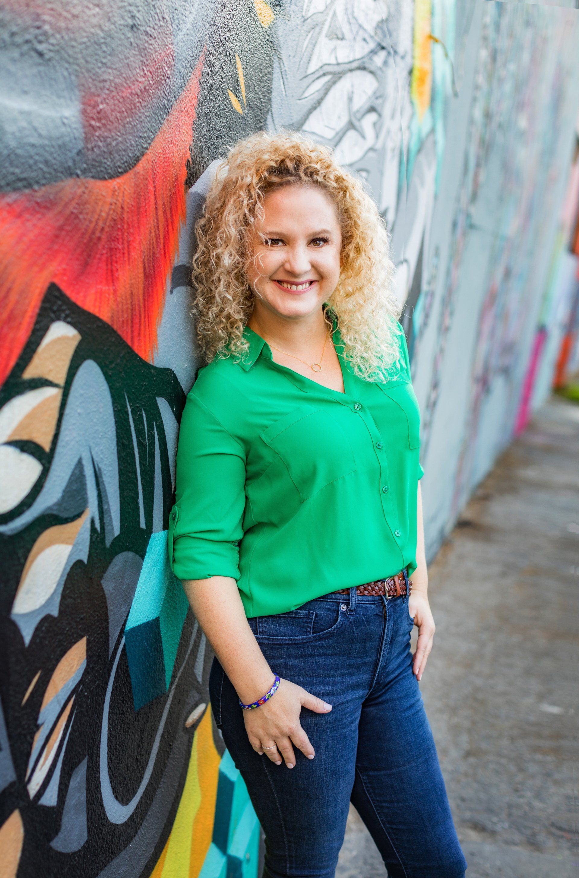 A woman in a green shirt is leaning against a graffiti wall.