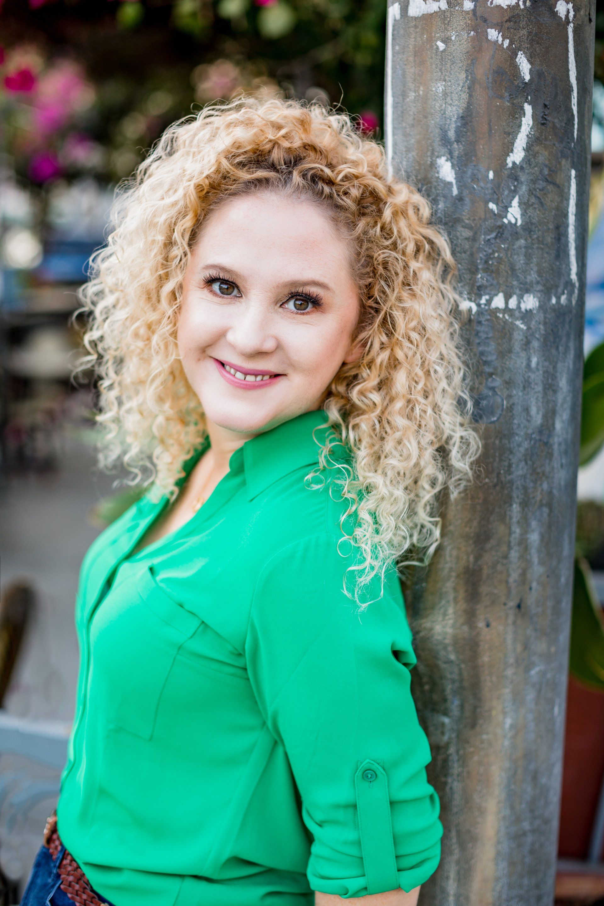 A woman with curly hair is leaning against a pole and smiling.