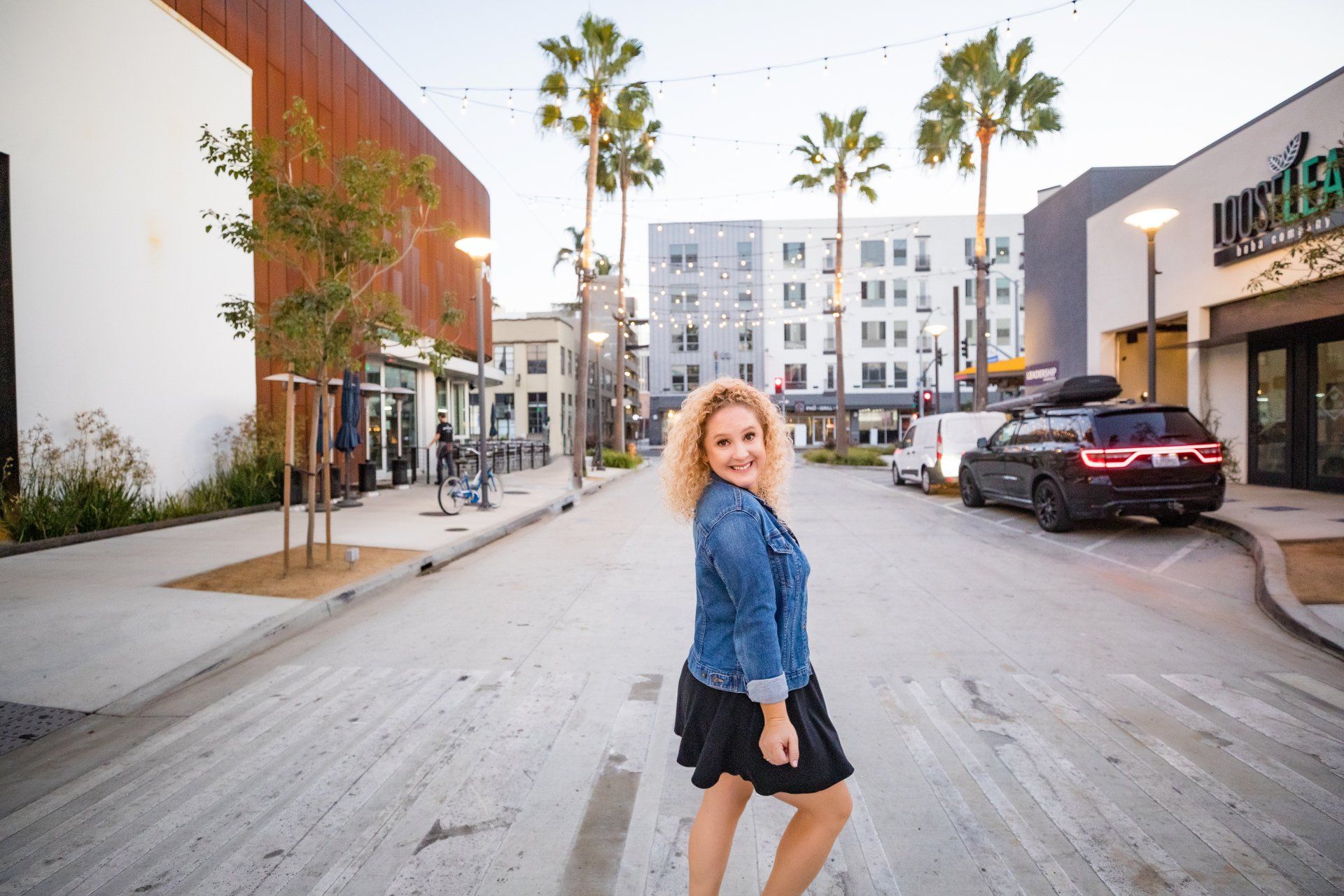 A woman is standing on the side of a street in front of a building.
