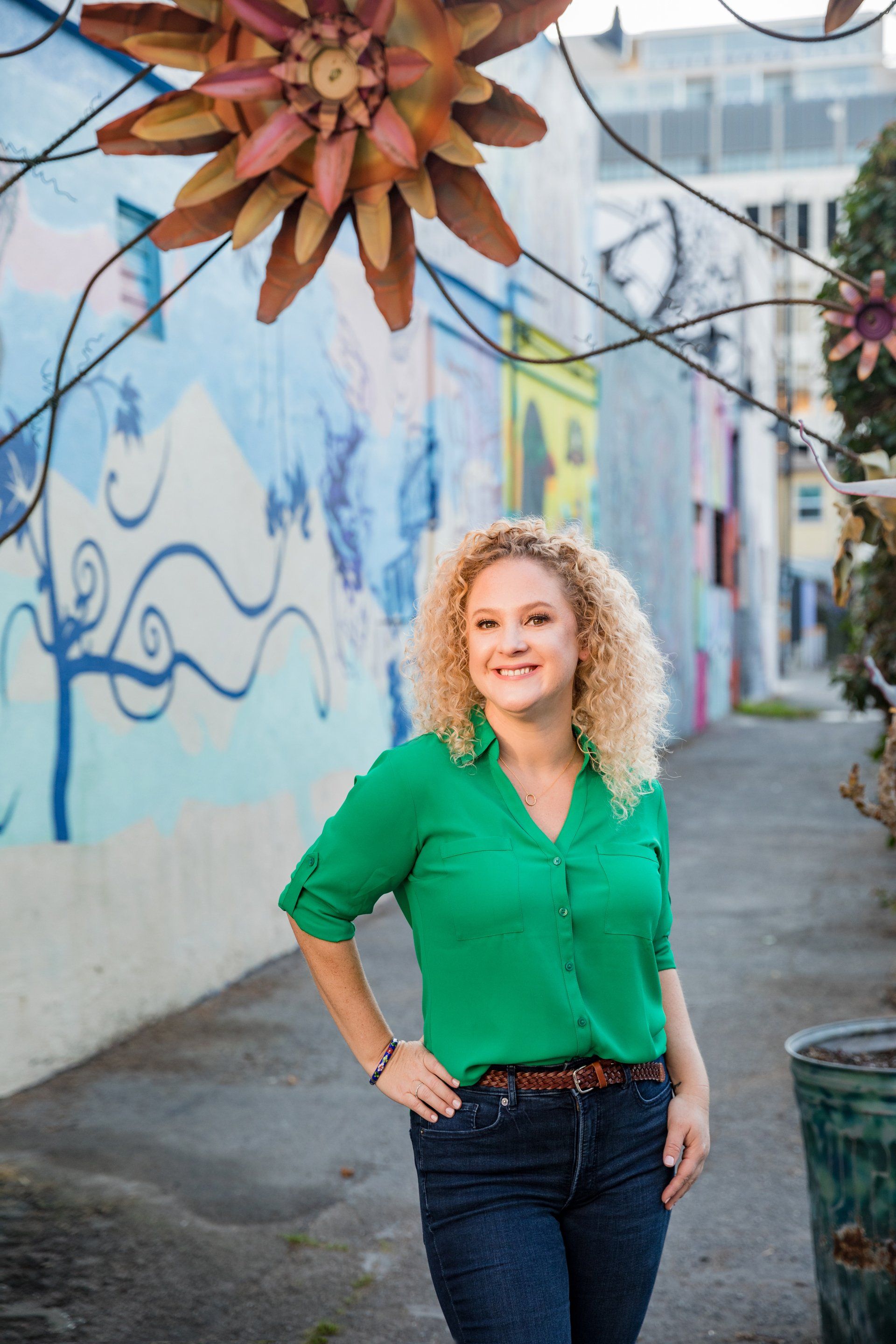 A woman in a green shirt is standing in front of a mural on a wall.