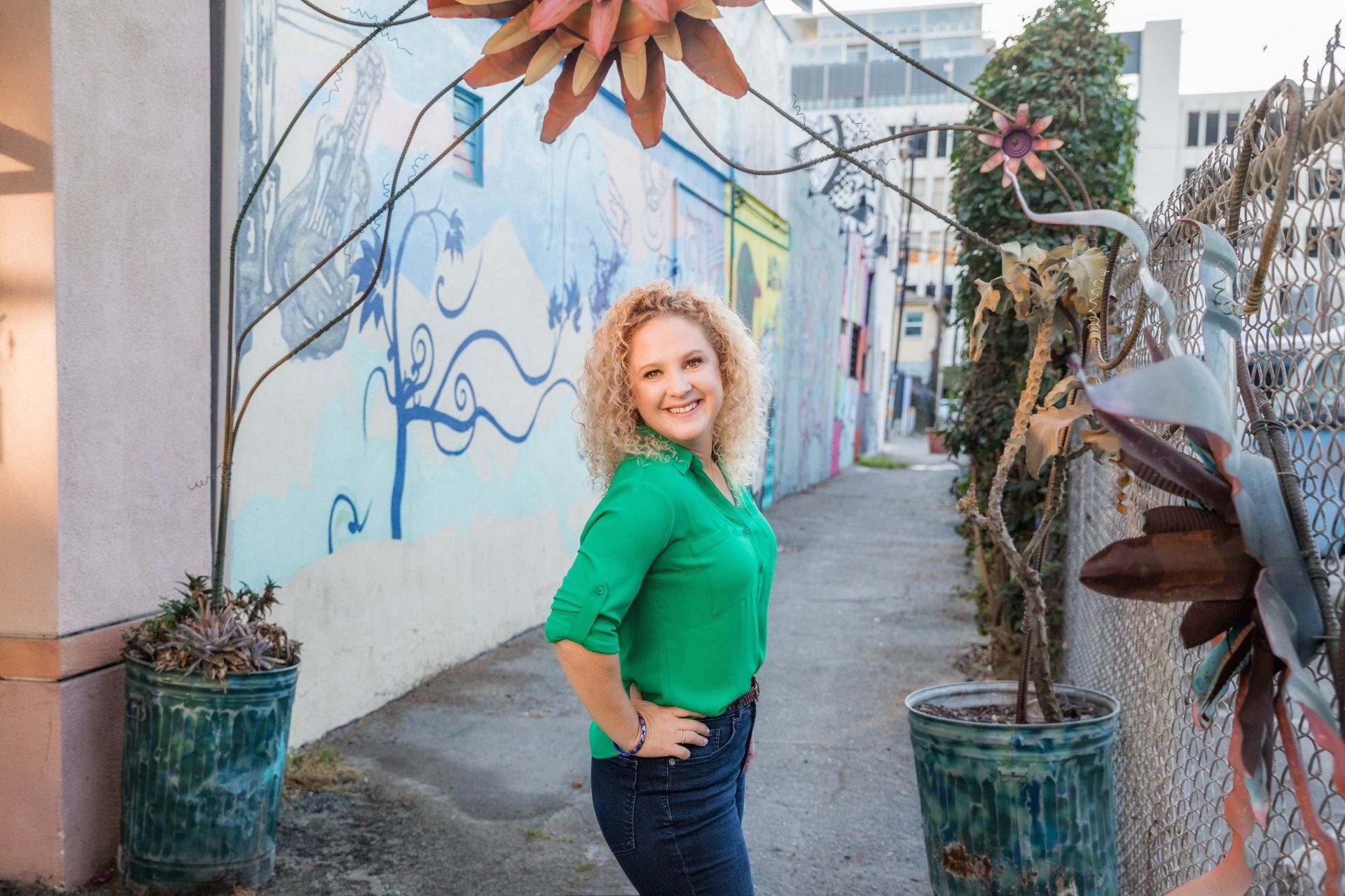 A woman in a green shirt is standing in front of a mural on a wall.