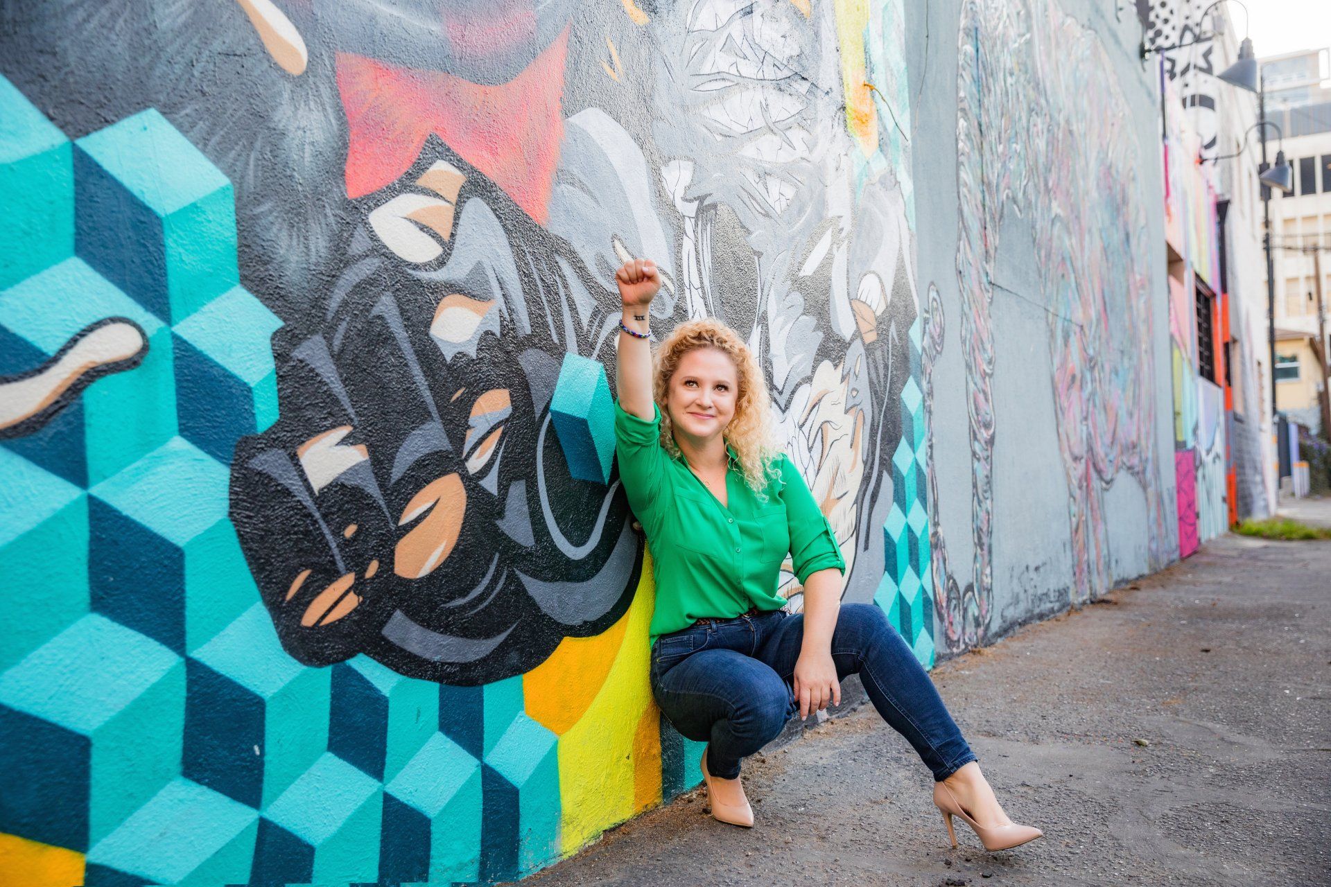 A woman is kneeling down in front of a colorful graffiti wall.