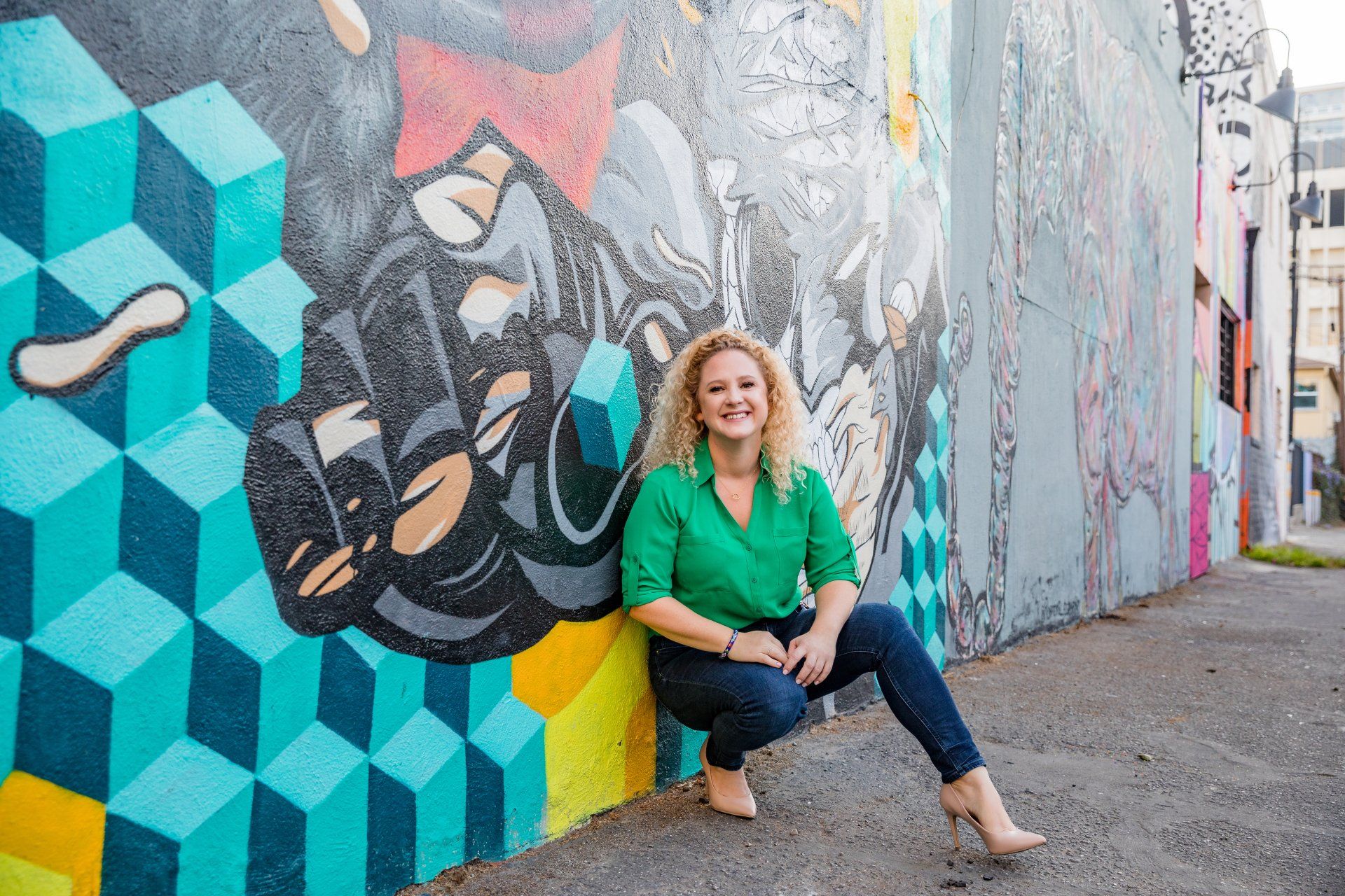 A woman is kneeling down in front of a colorful graffiti wall.