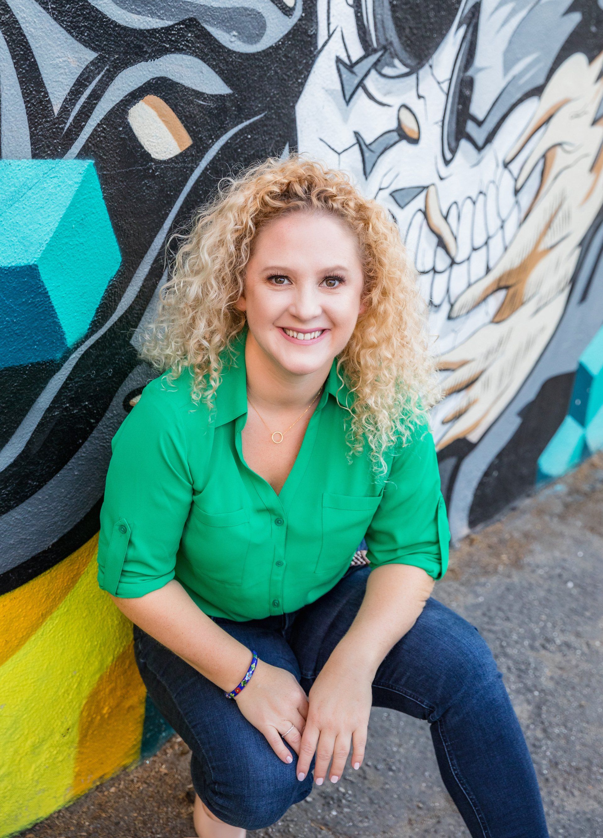A woman in a green shirt is kneeling in front of a graffiti wall.