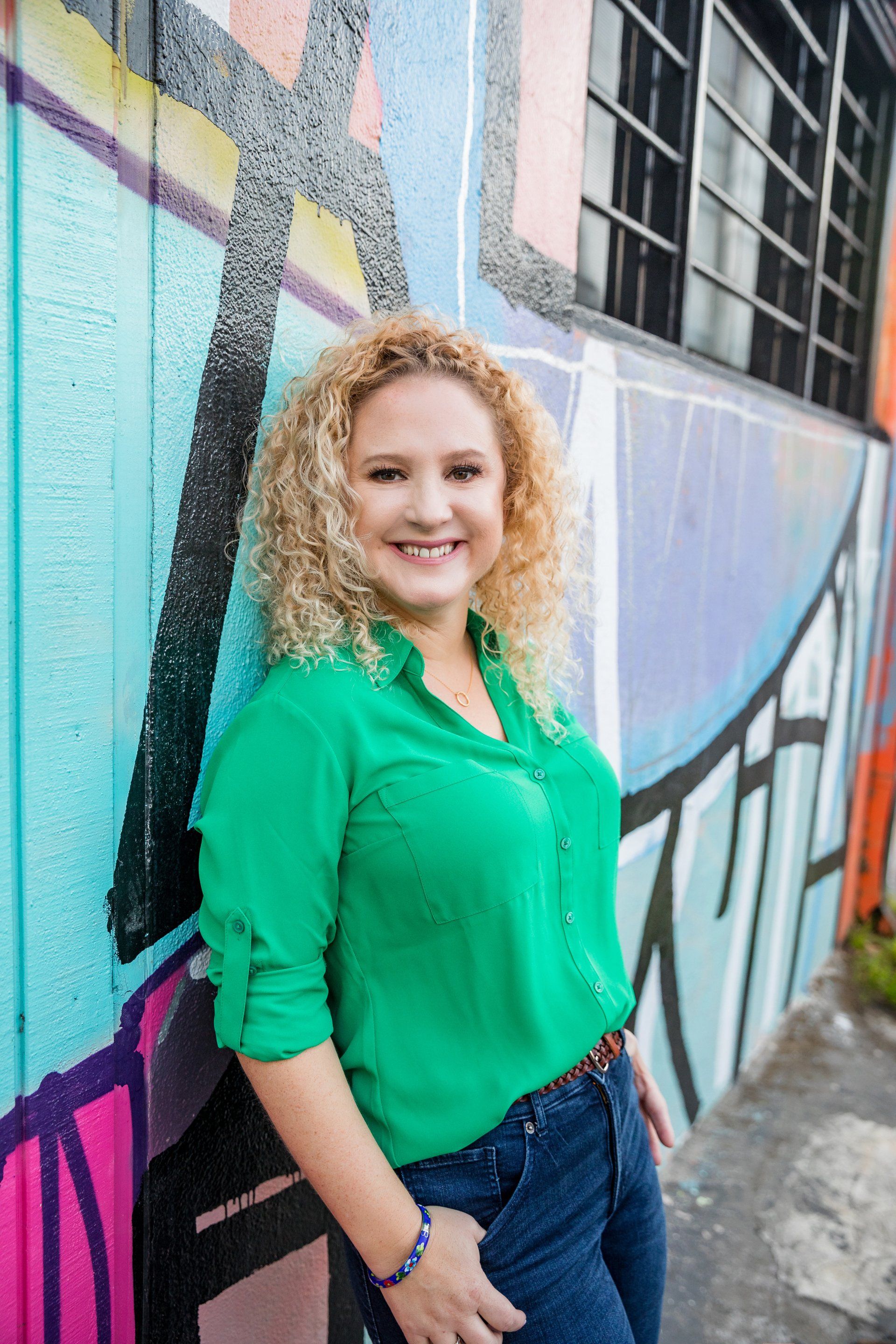 A woman in a green shirt is standing in front of a graffiti wall.