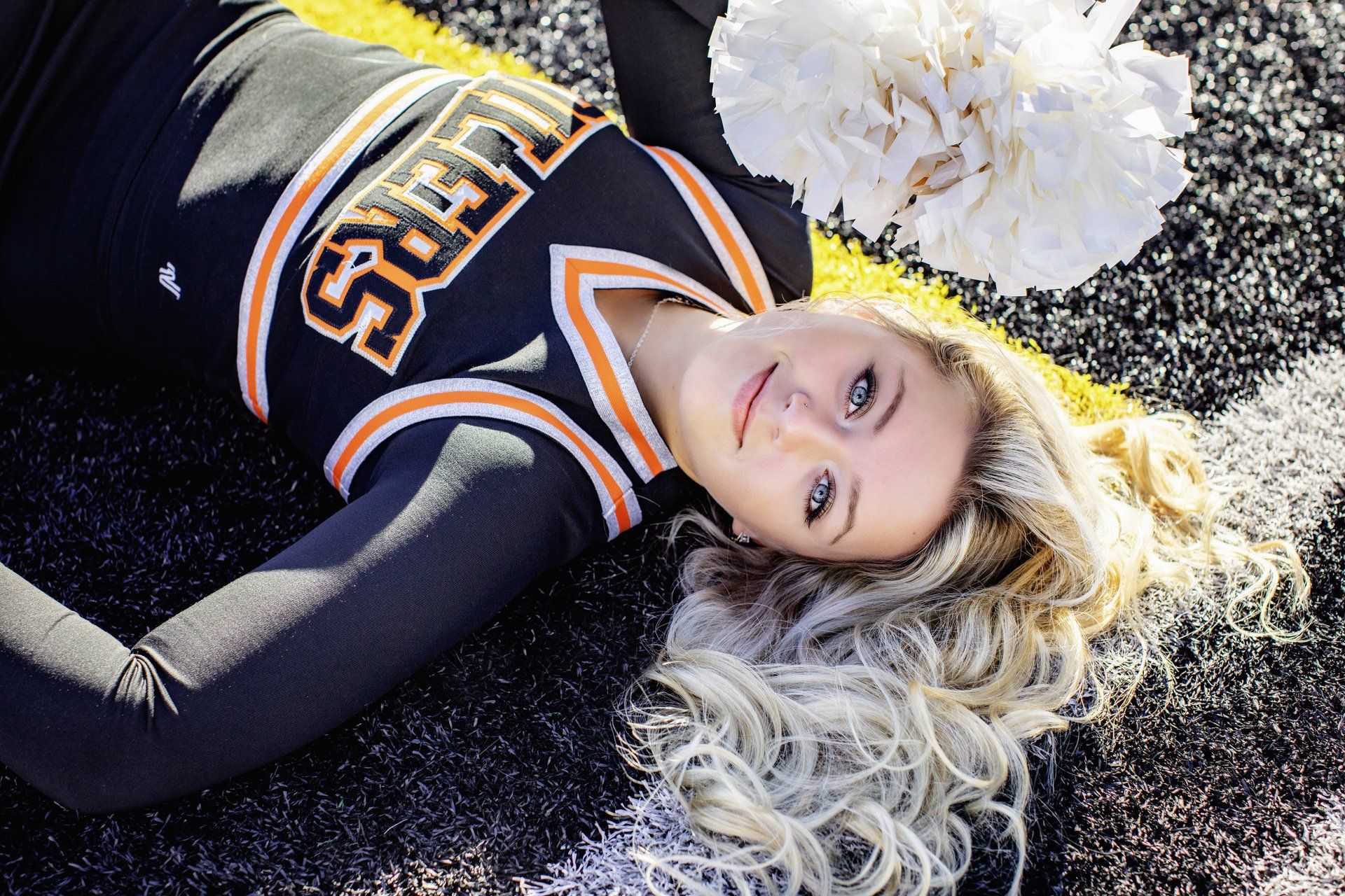 A cheerleader is laying on the ground holding pom poms.