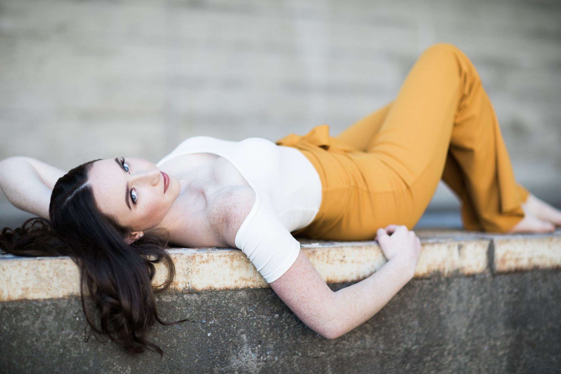 A woman in a white top and yellow pants is laying on a wall.