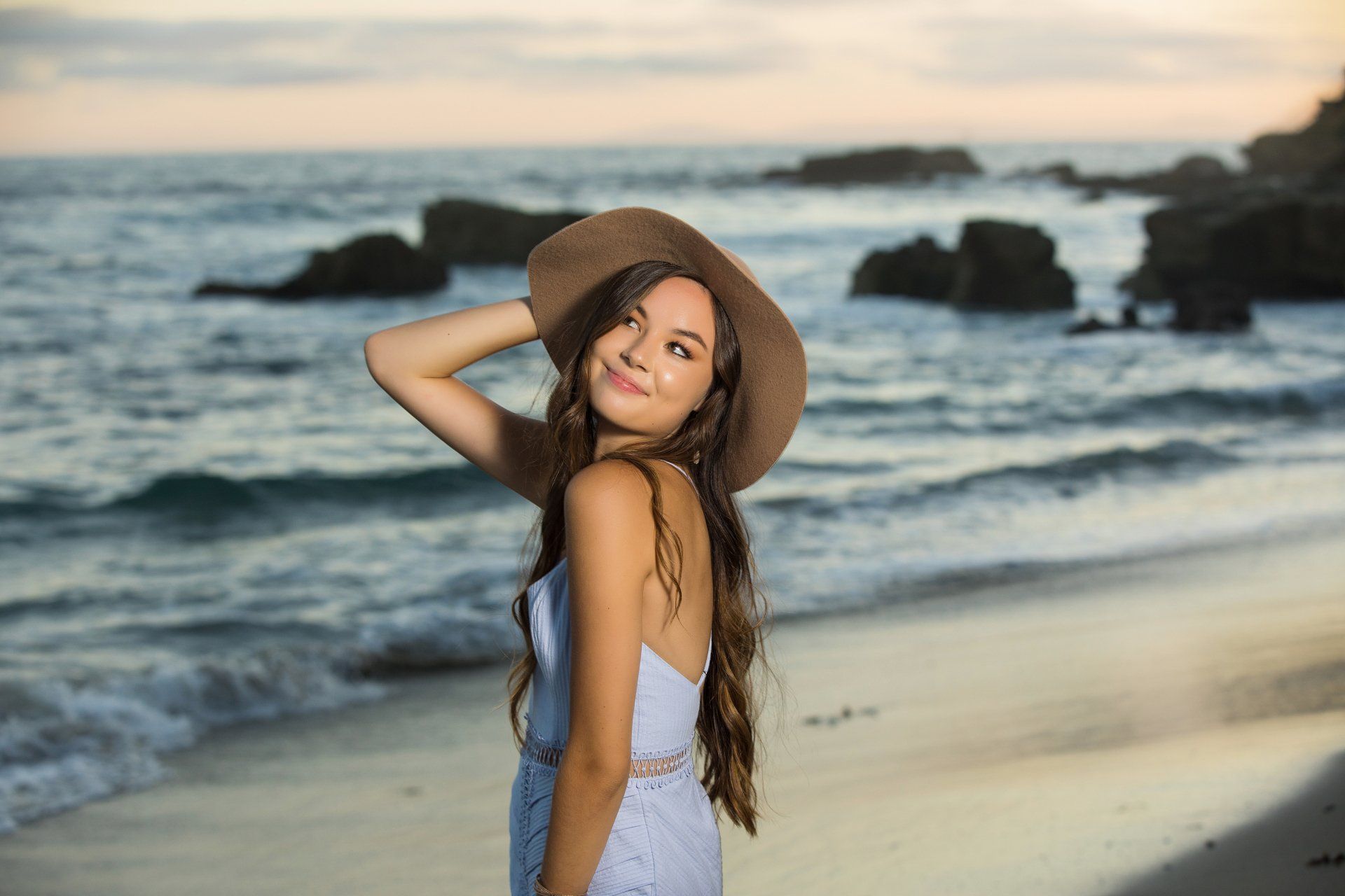 A woman in a hat is standing on a beach.