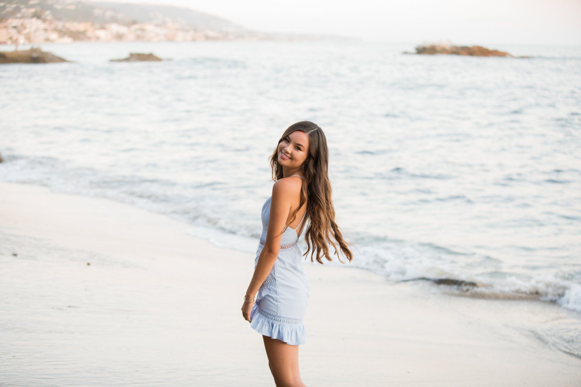 A woman in a blue dress is standing on a beach near the ocean.