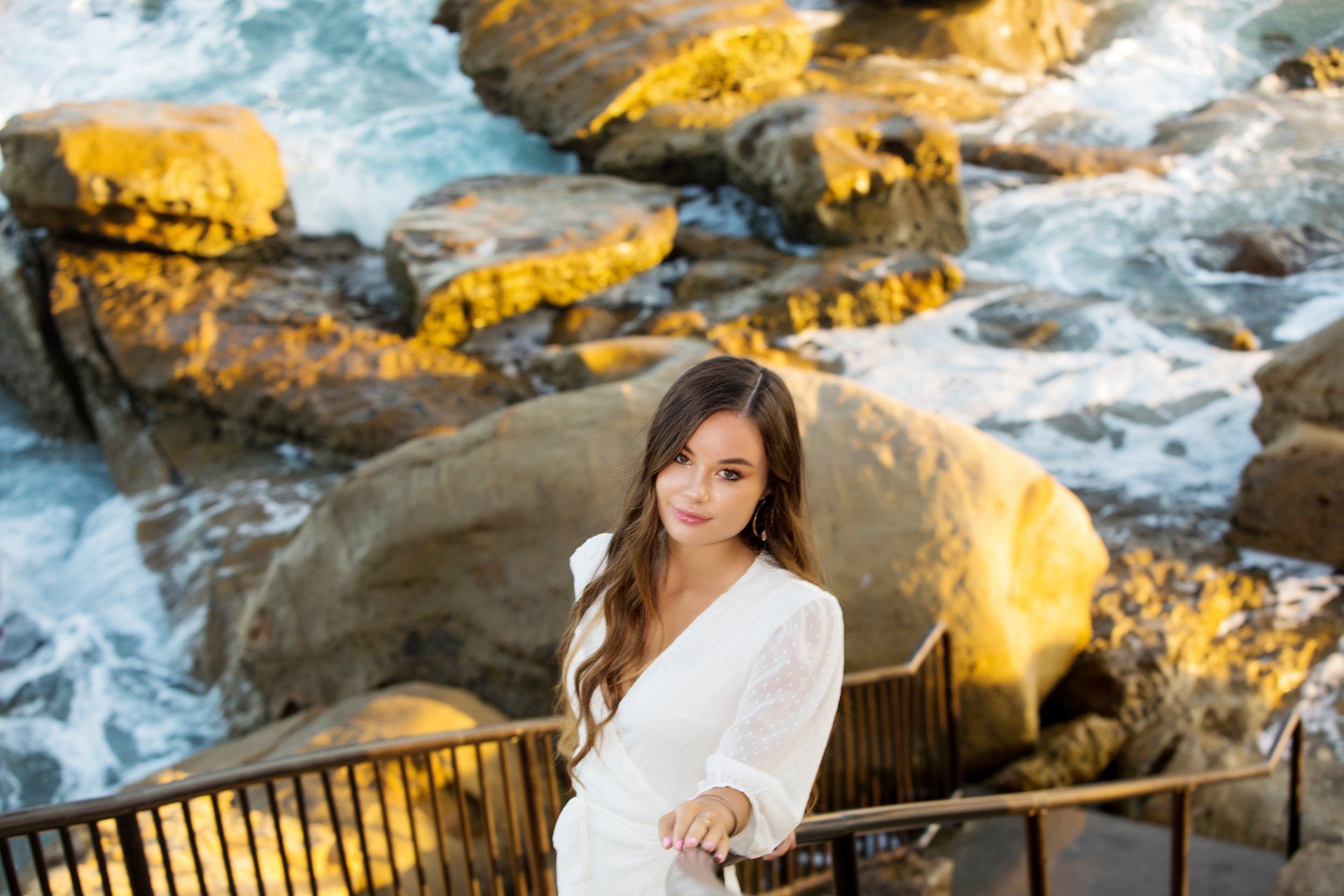 A woman in a white dress is standing on a bridge overlooking the ocean.
