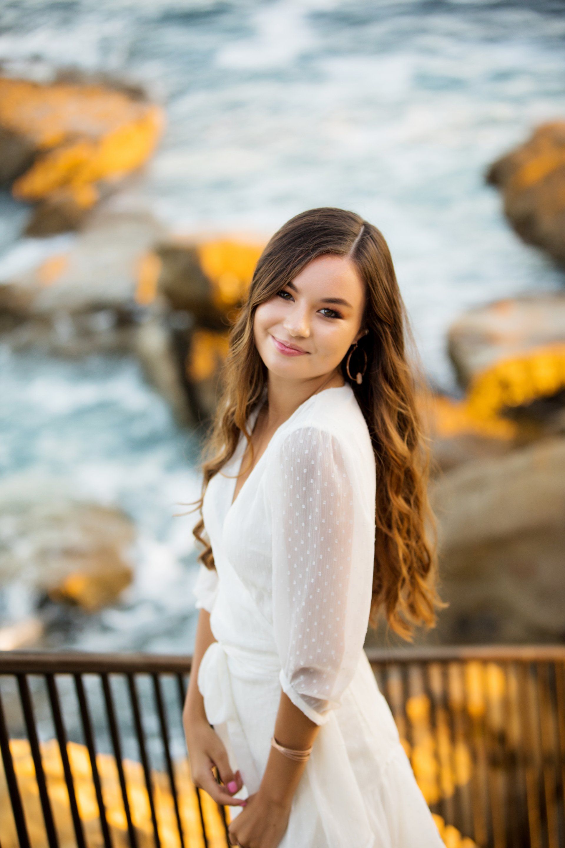 A woman in a white dress is standing on a bridge overlooking the ocean.