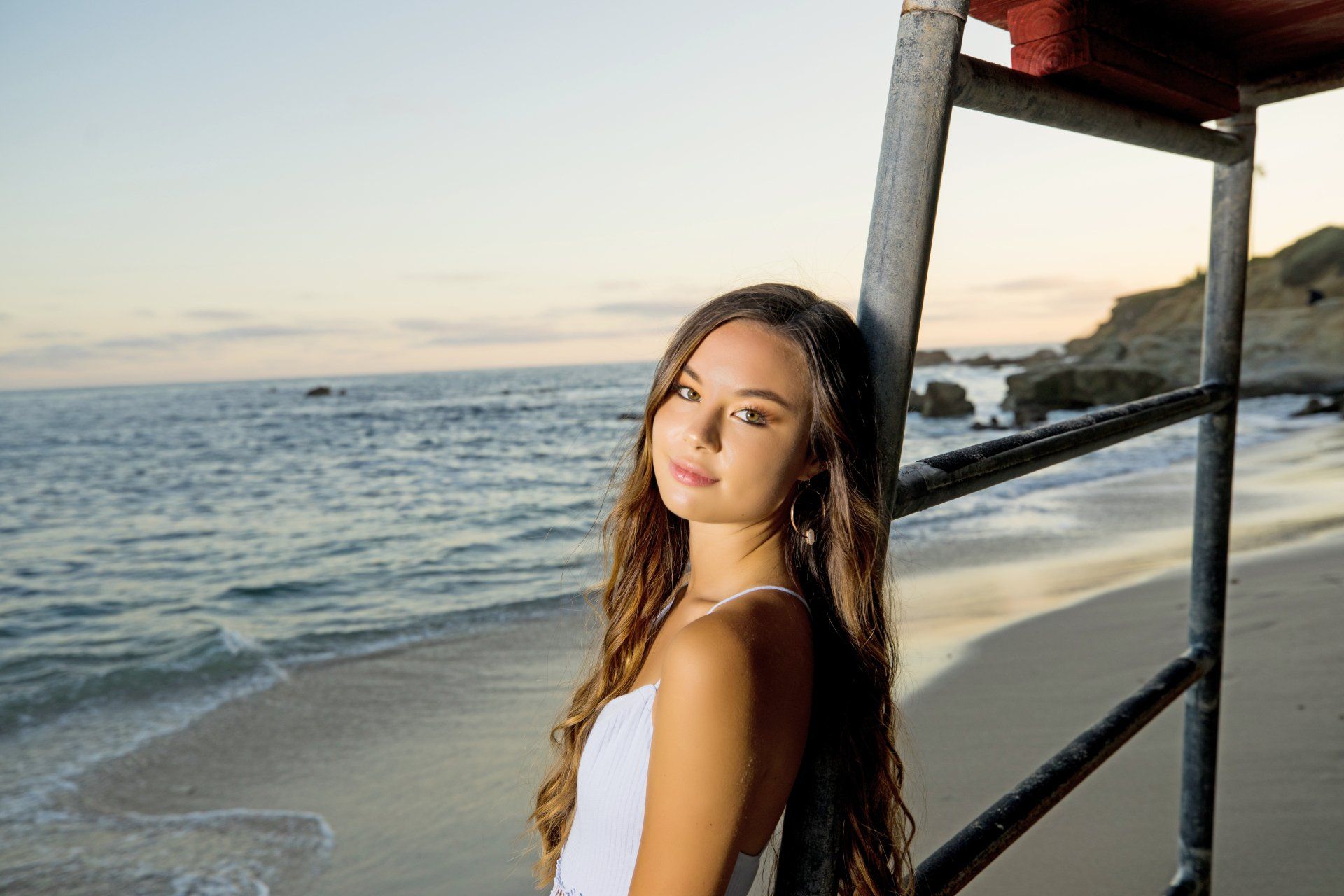 A woman in a white dress is standing on a beach next to a lifeguard tower.