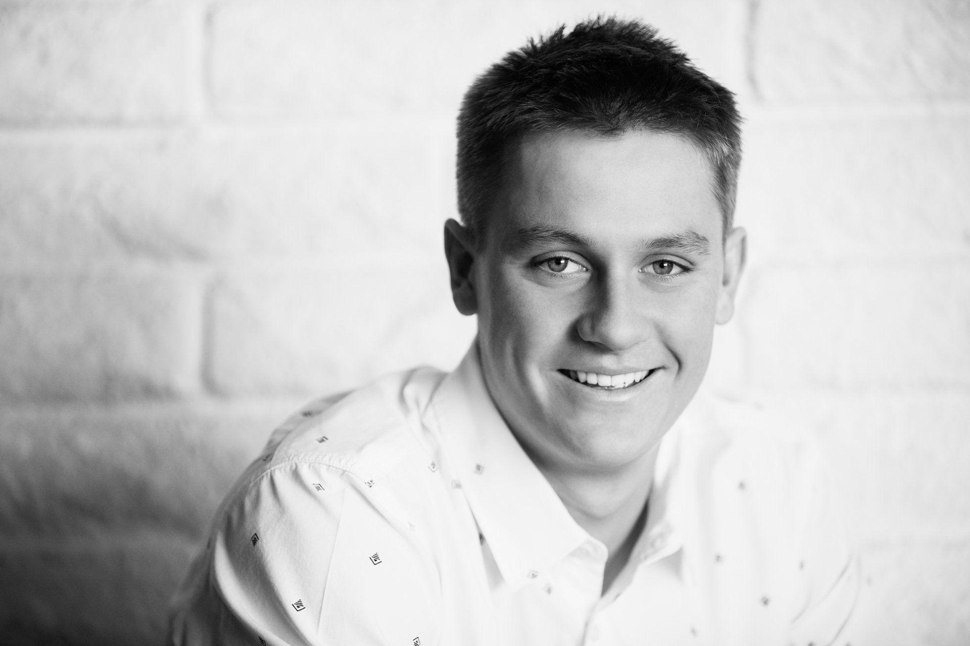 A young man in a white shirt is smiling in a black and white photo.