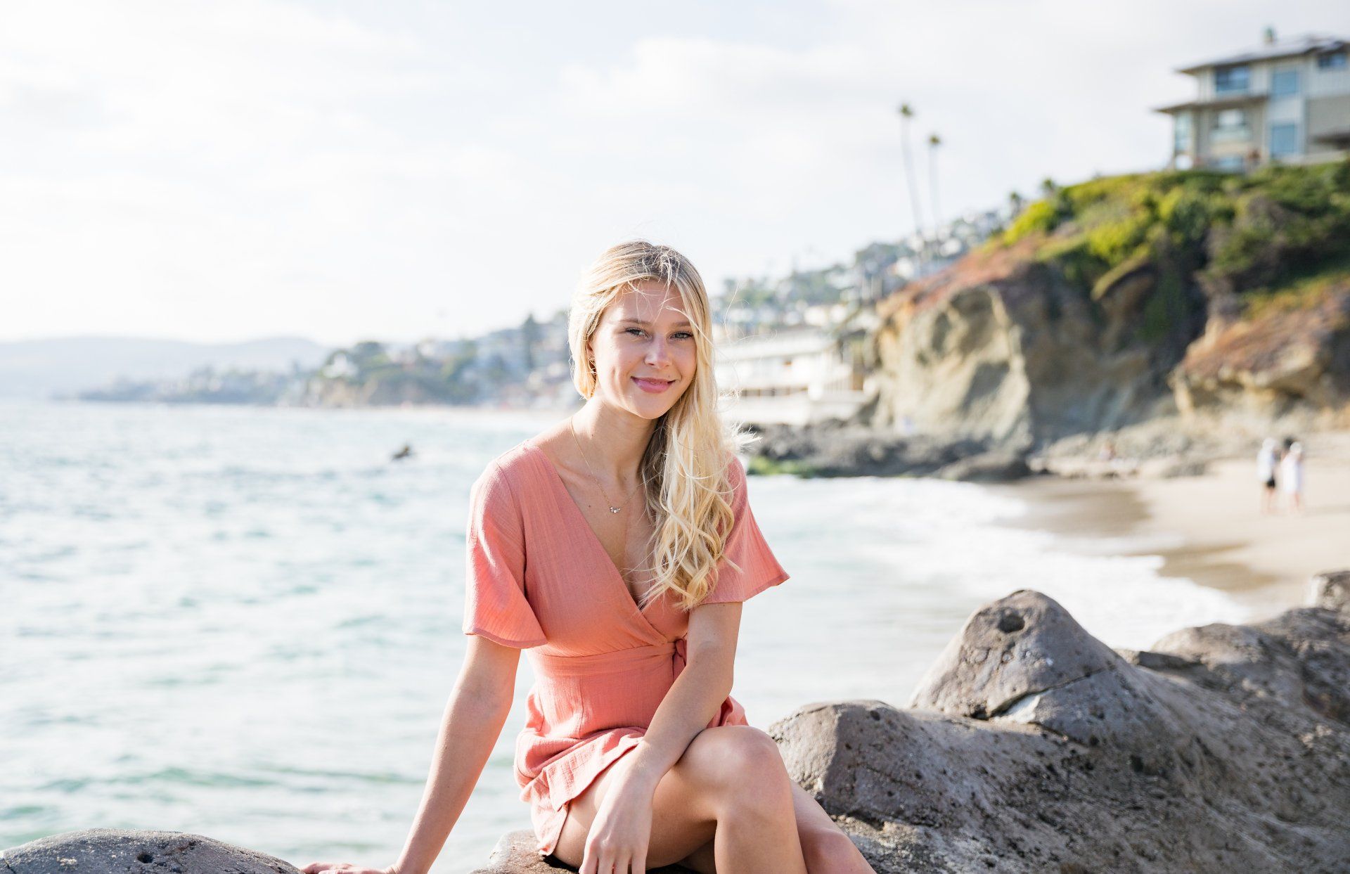 A woman in a pink dress is sitting on a rock near the ocean.