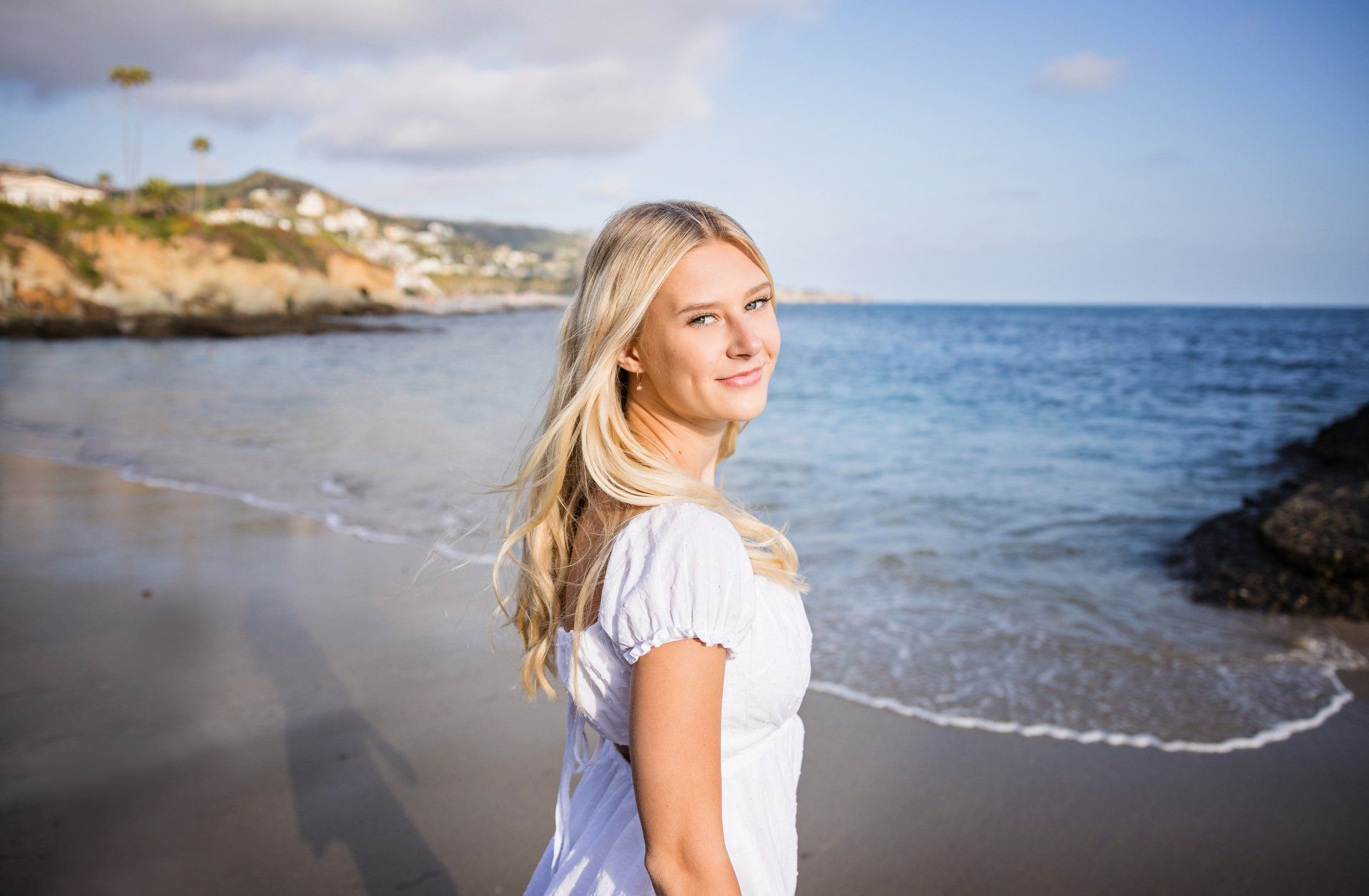 A woman in a white dress is standing on a beach near the ocean.