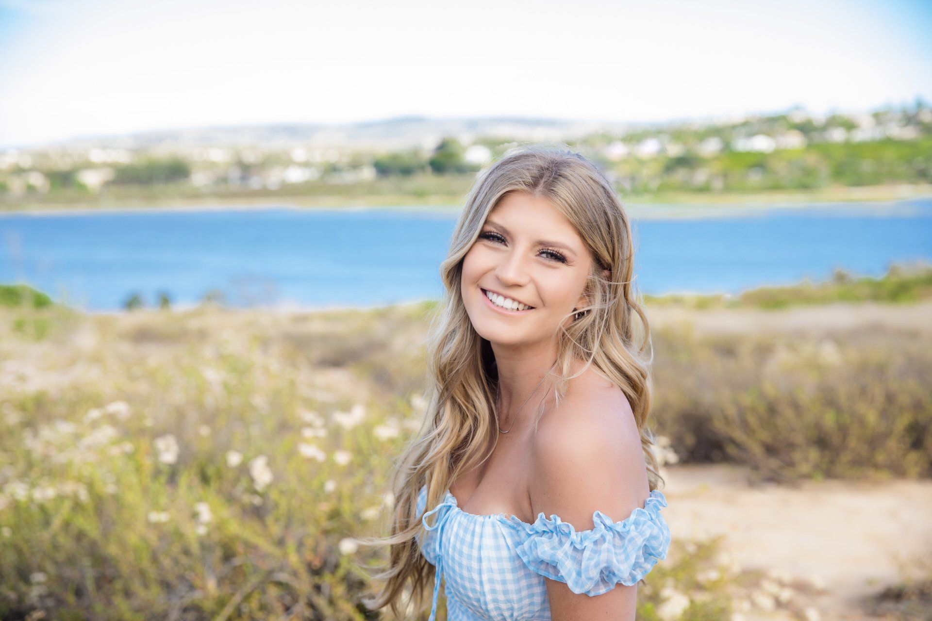 A young woman is standing in a field with a lake in the background.