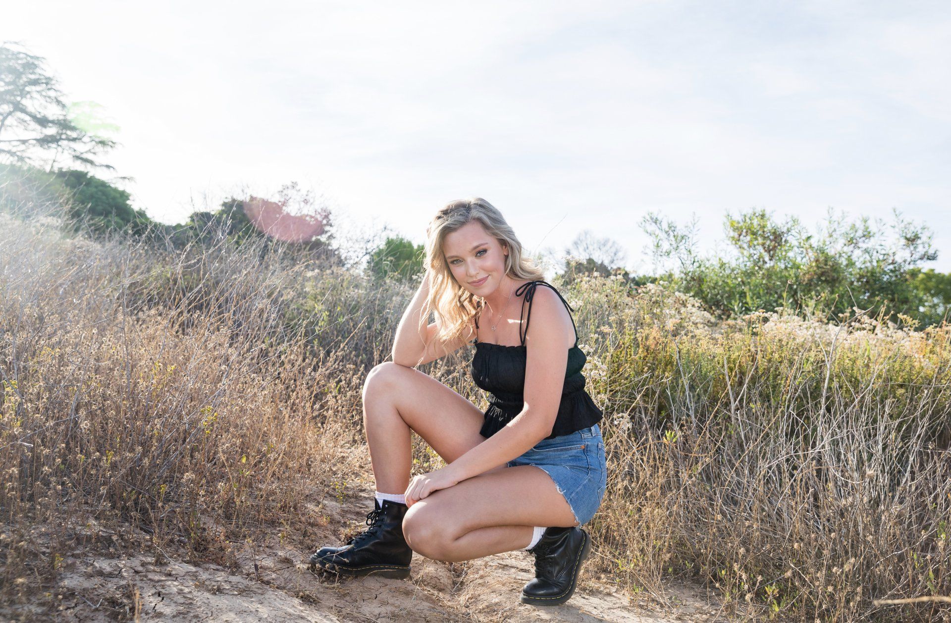 A woman is squatting down in a field of tall grass.