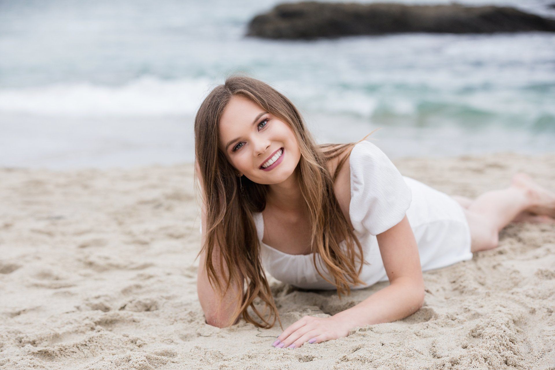 A woman in a white dress is laying on the beach.