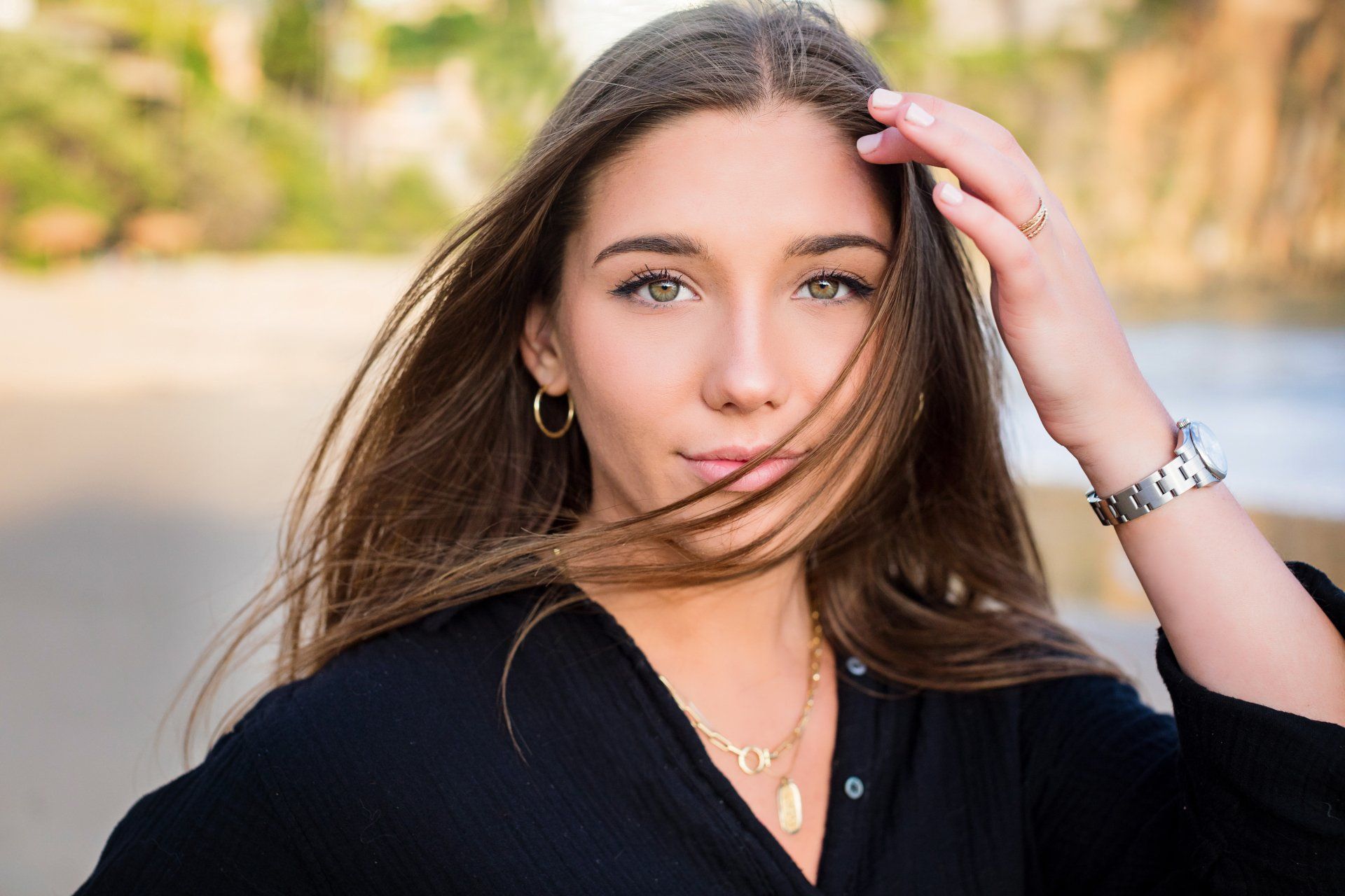 A woman in a black shirt is touching her hair.