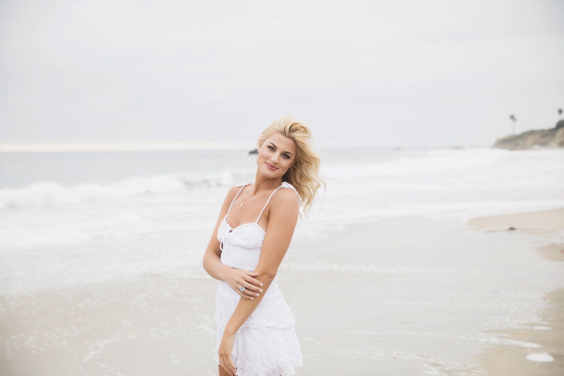 A woman in a white dress is standing on the beach.
