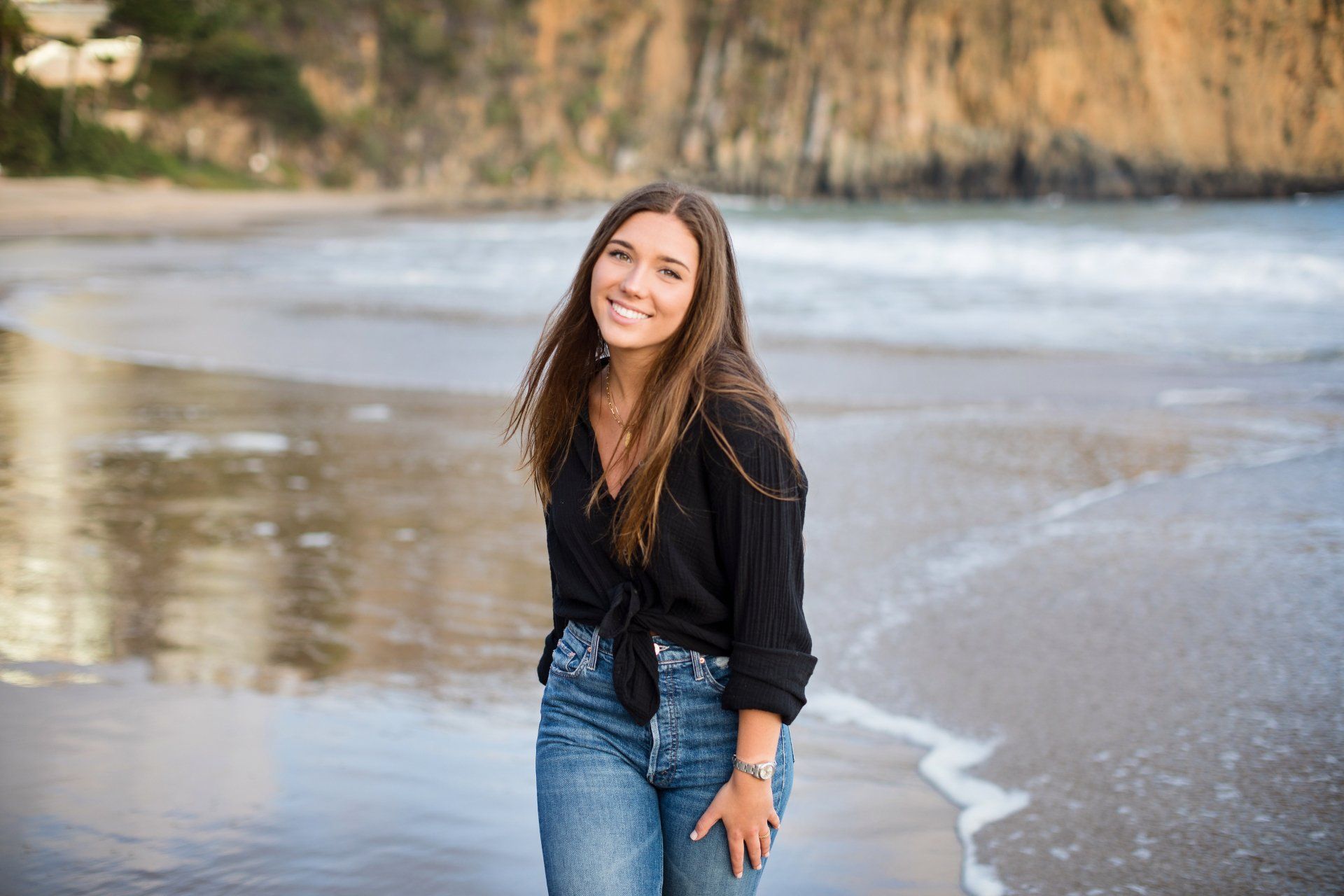 A woman in a black shirt and jeans is standing on a beach.