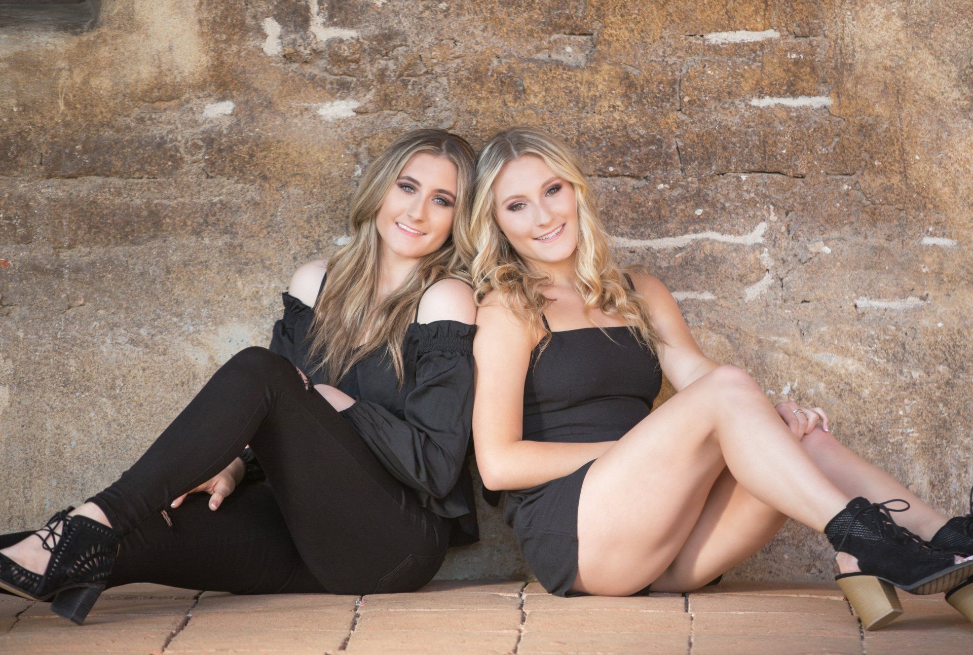Two women are sitting next to each other in front of a brick wall.