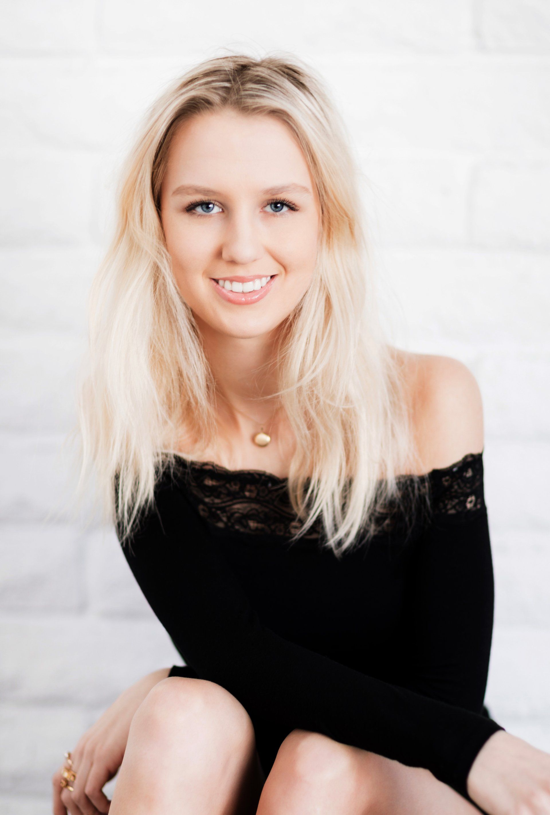 The woman is wearing a black off the shoulder top and smiling.