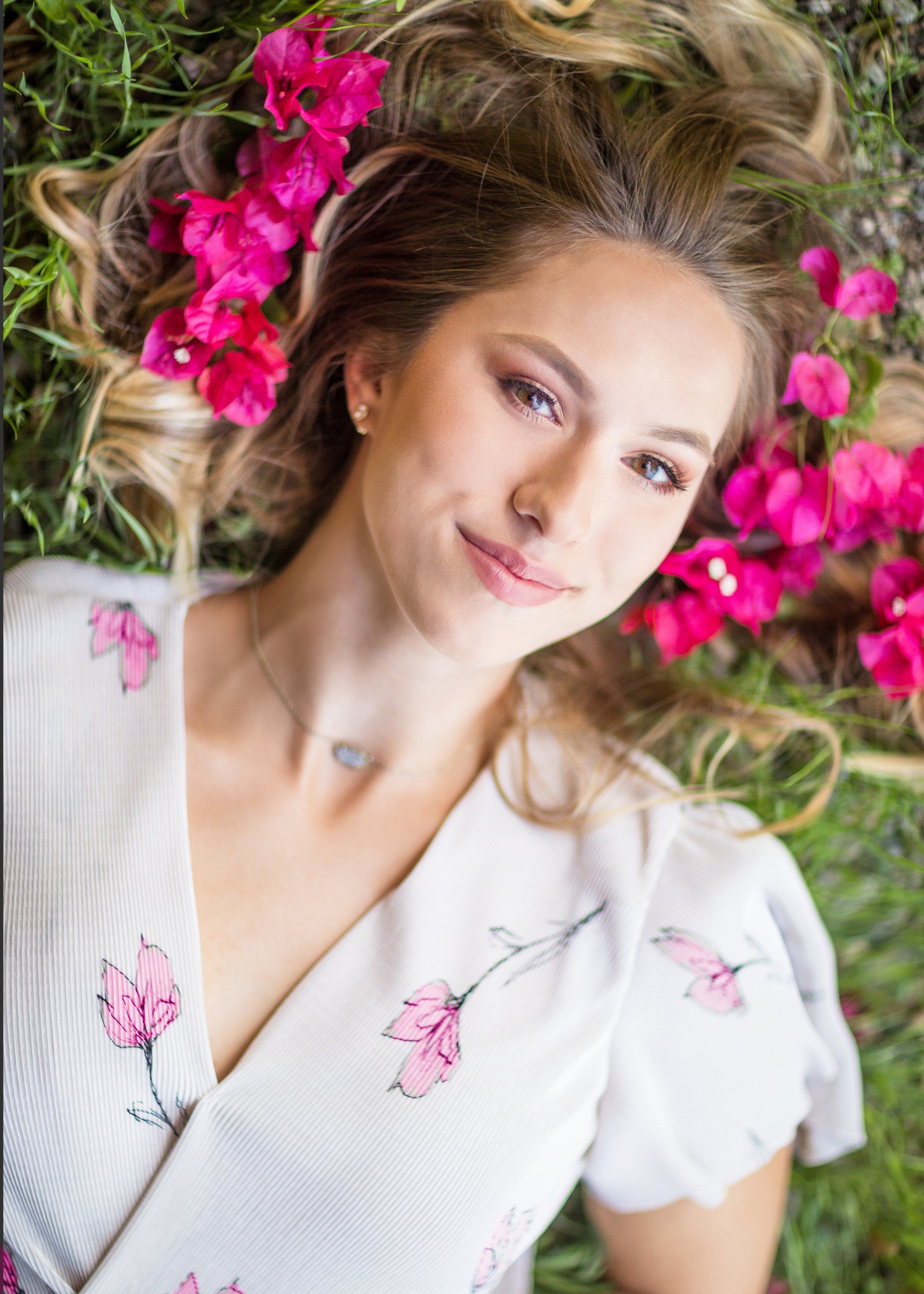 A woman is laying in the grass with pink flowers in her hair.