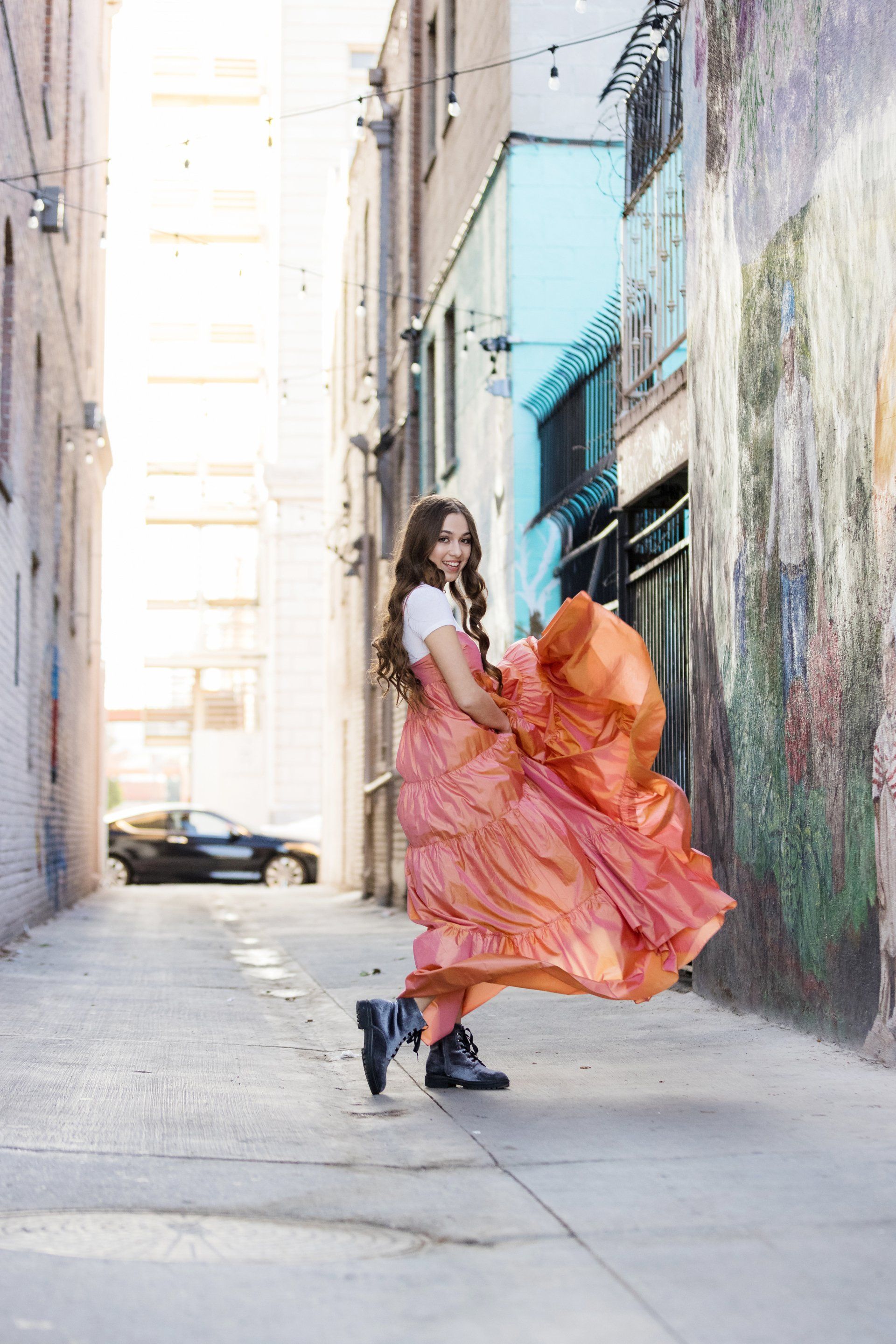 A woman in a long pink dress is standing in an alleyway.
