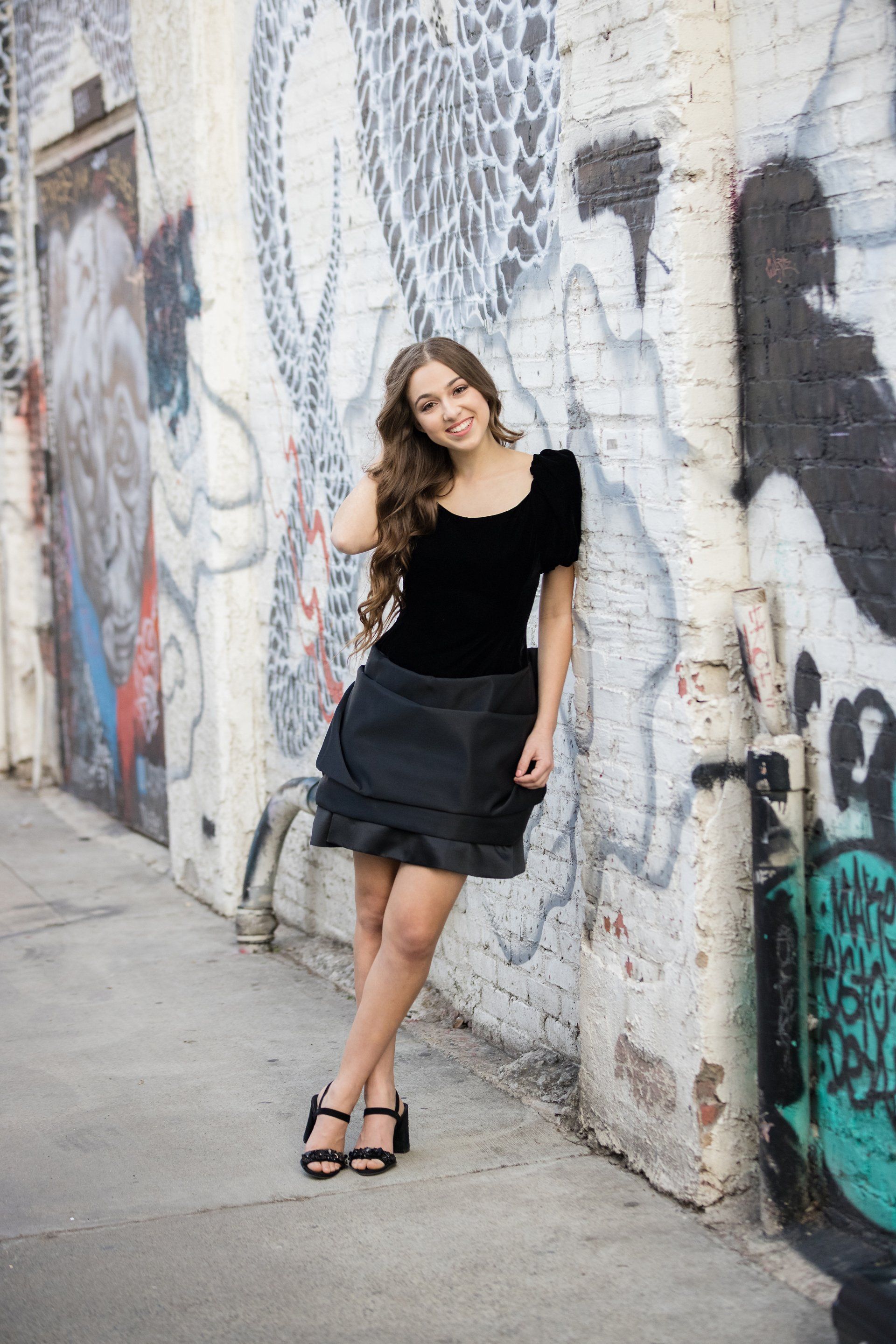 A woman is standing in front of a graffiti covered wall.