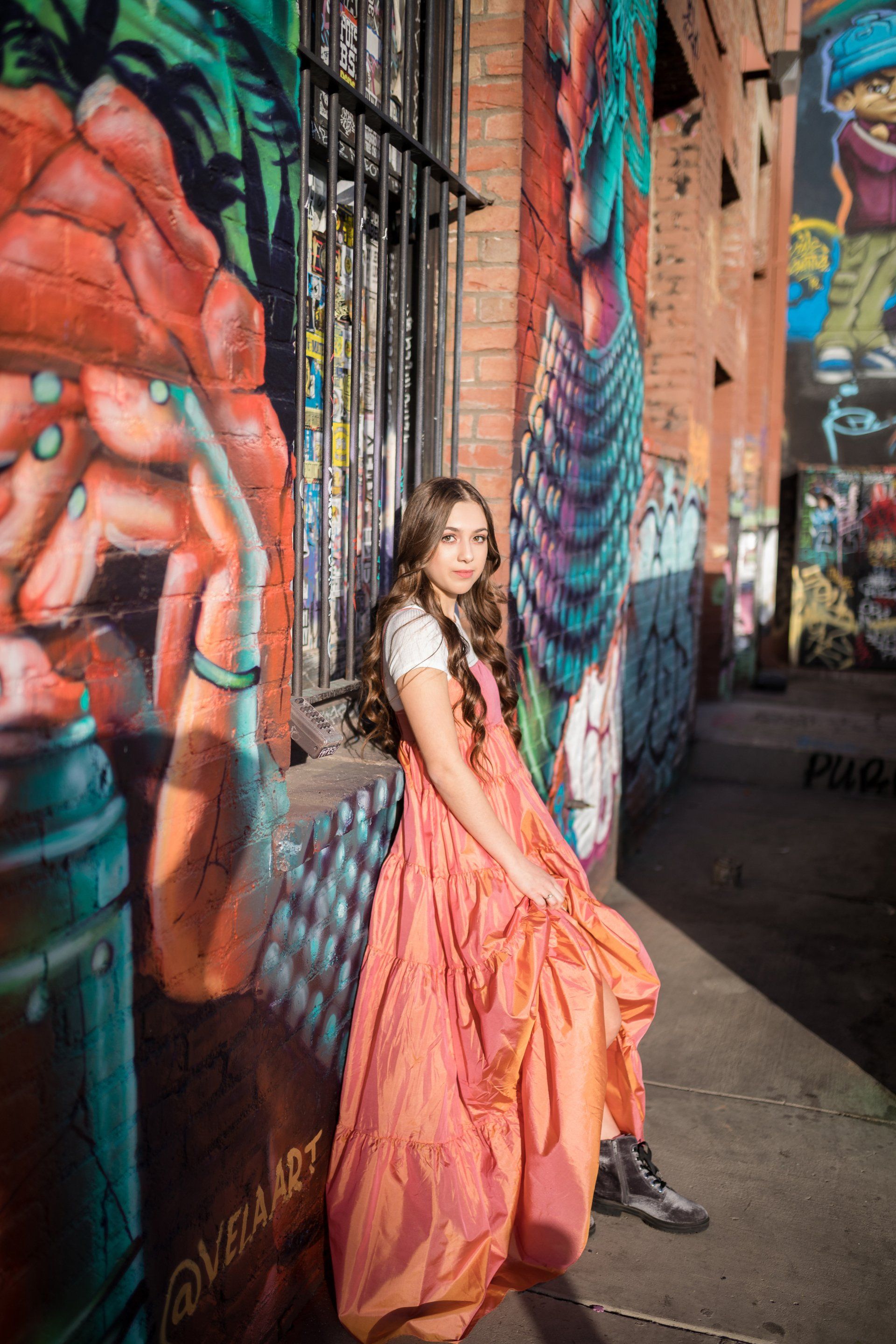 A woman in a long dress is standing in front of a graffiti wall.