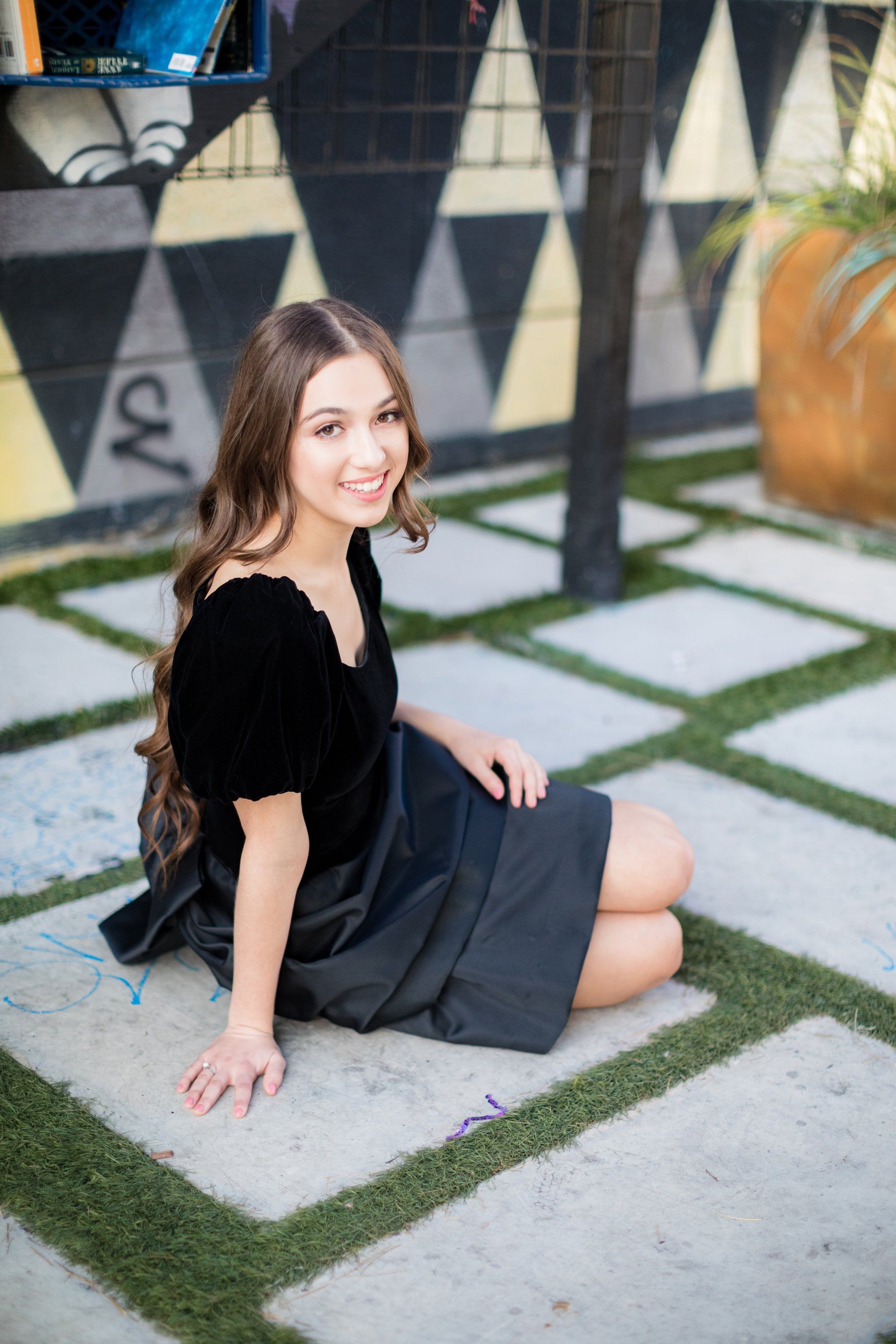 A young woman in a black dress is sitting on the ground.