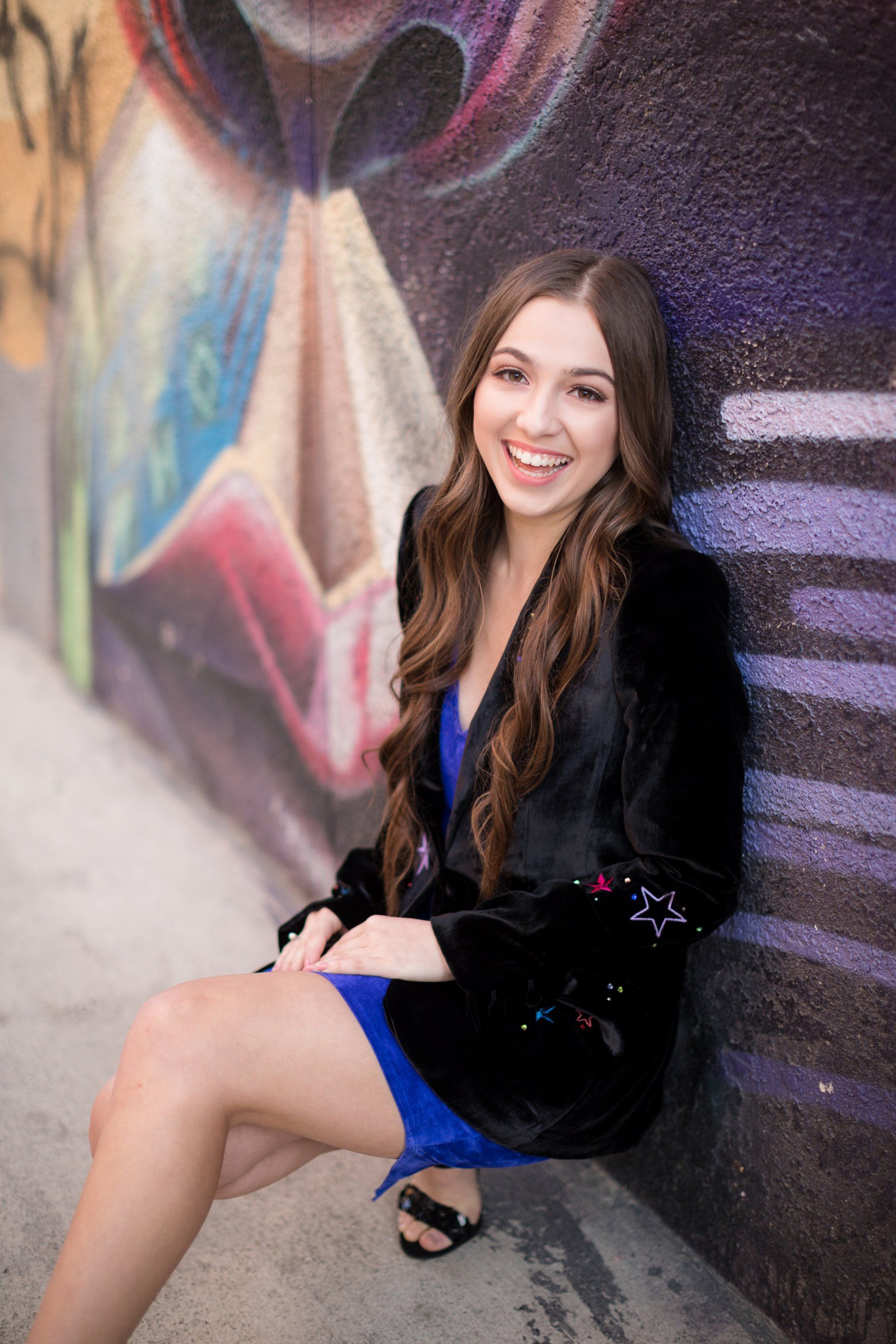A woman in a blue dress is sitting in front of a graffiti wall.