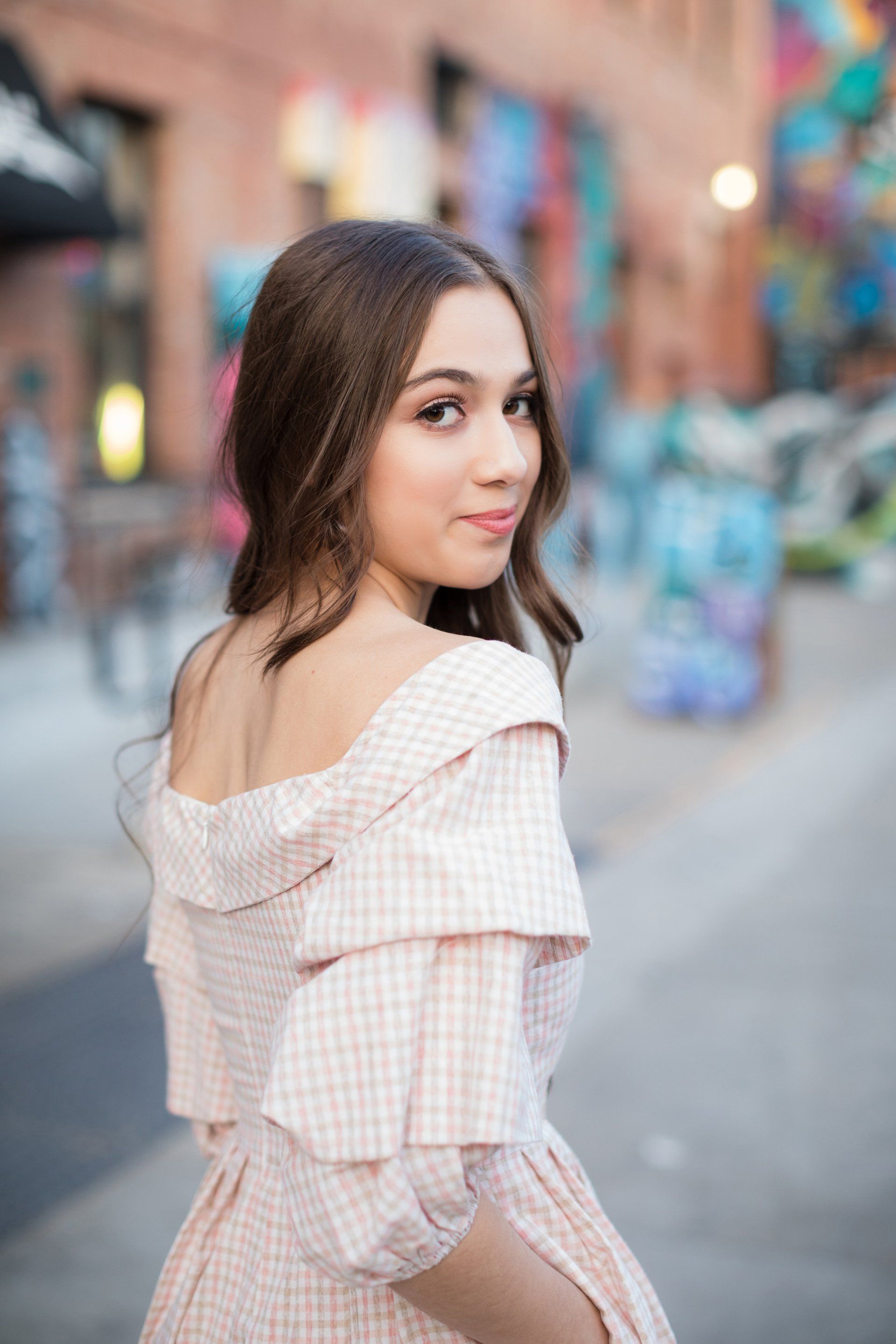 A young woman in a pink dress is standing in front of a graffiti wall.