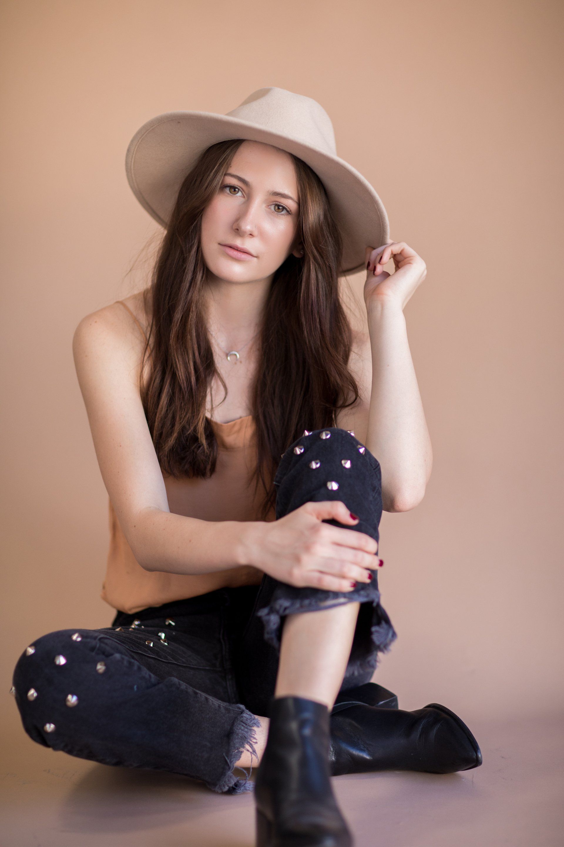 A woman wearing a hat and jeans is sitting on the floor.