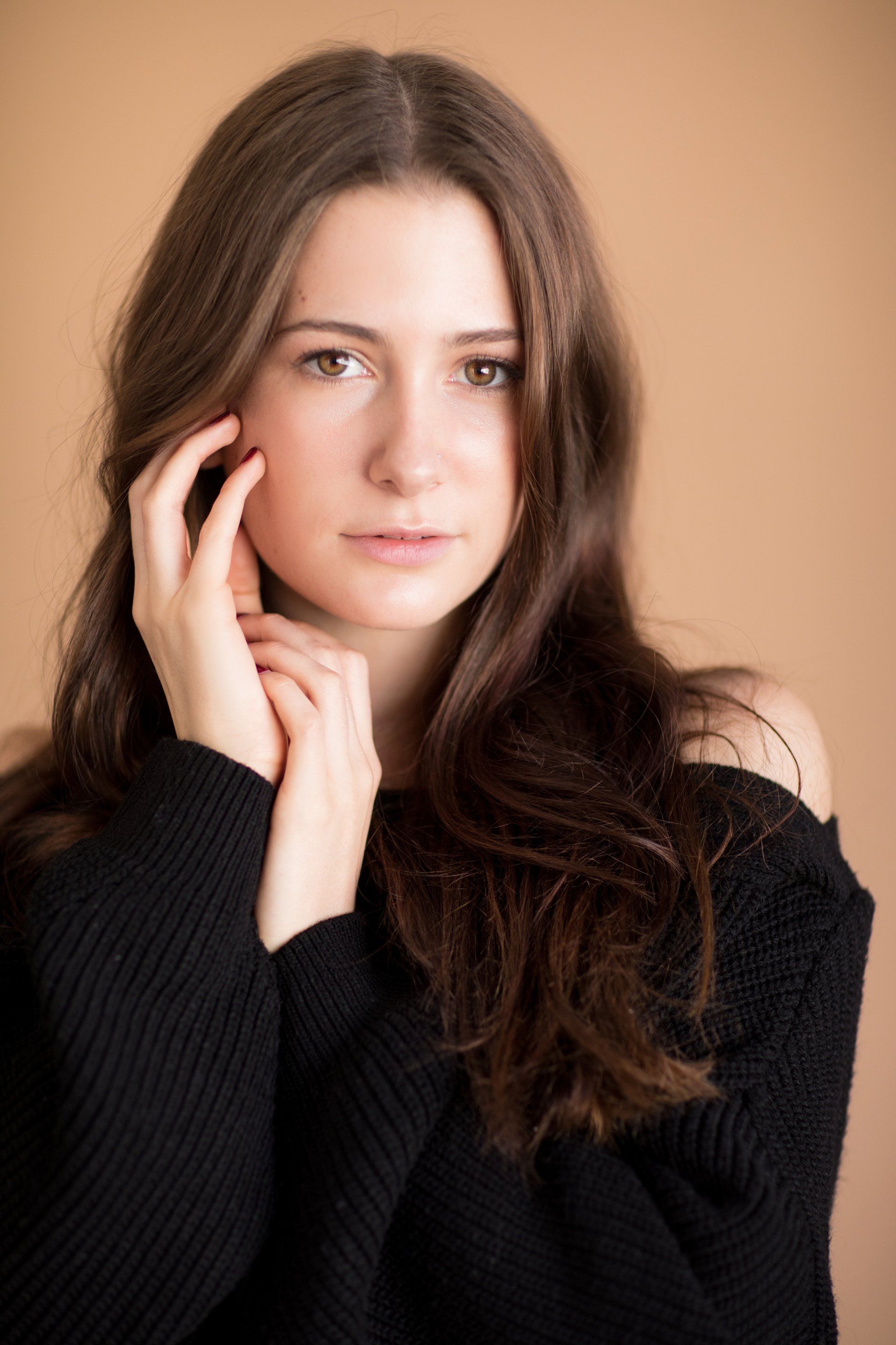 A young woman gently touches her face with both hands,