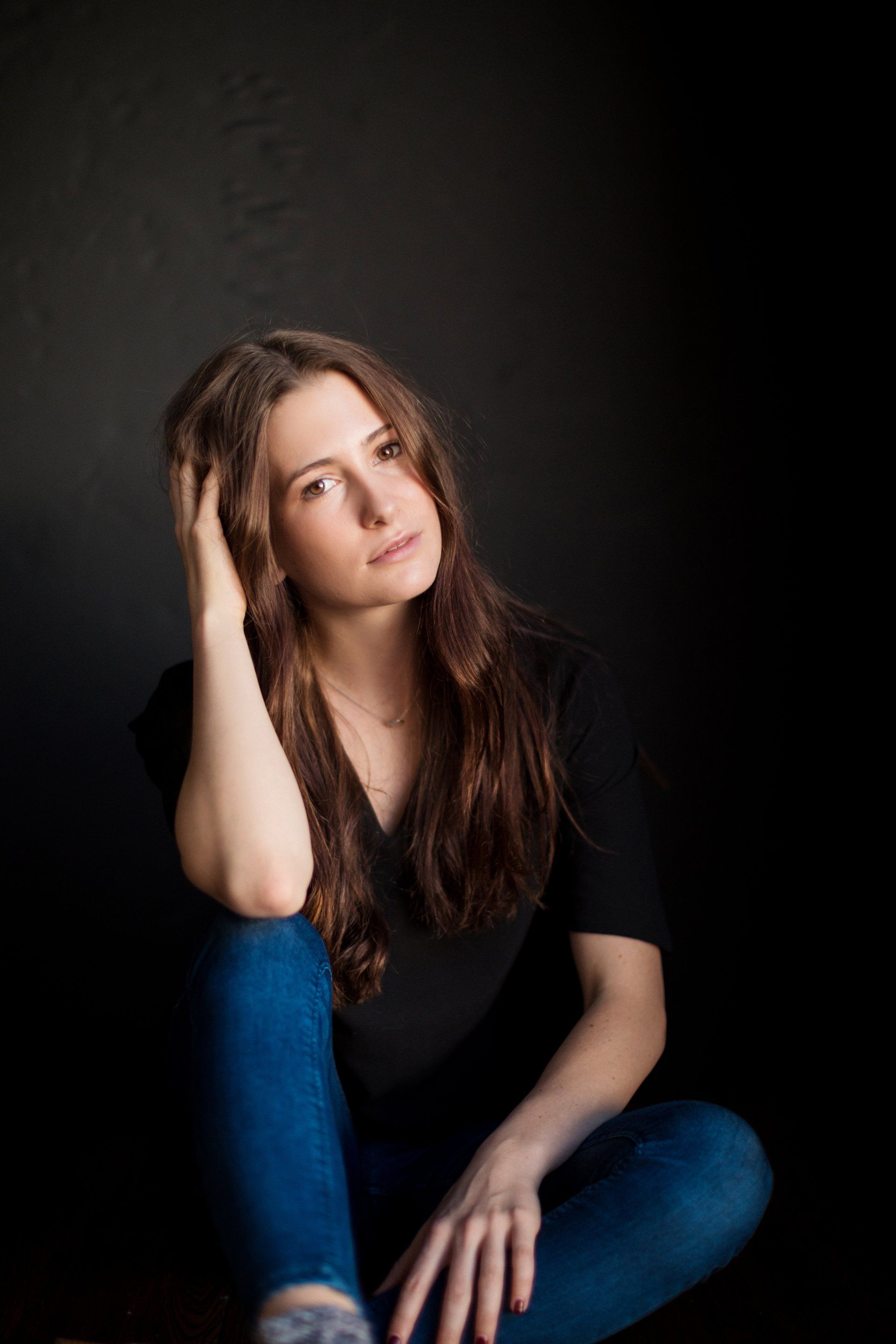 A woman is sitting on the floor with her legs crossed and her hand on her head.