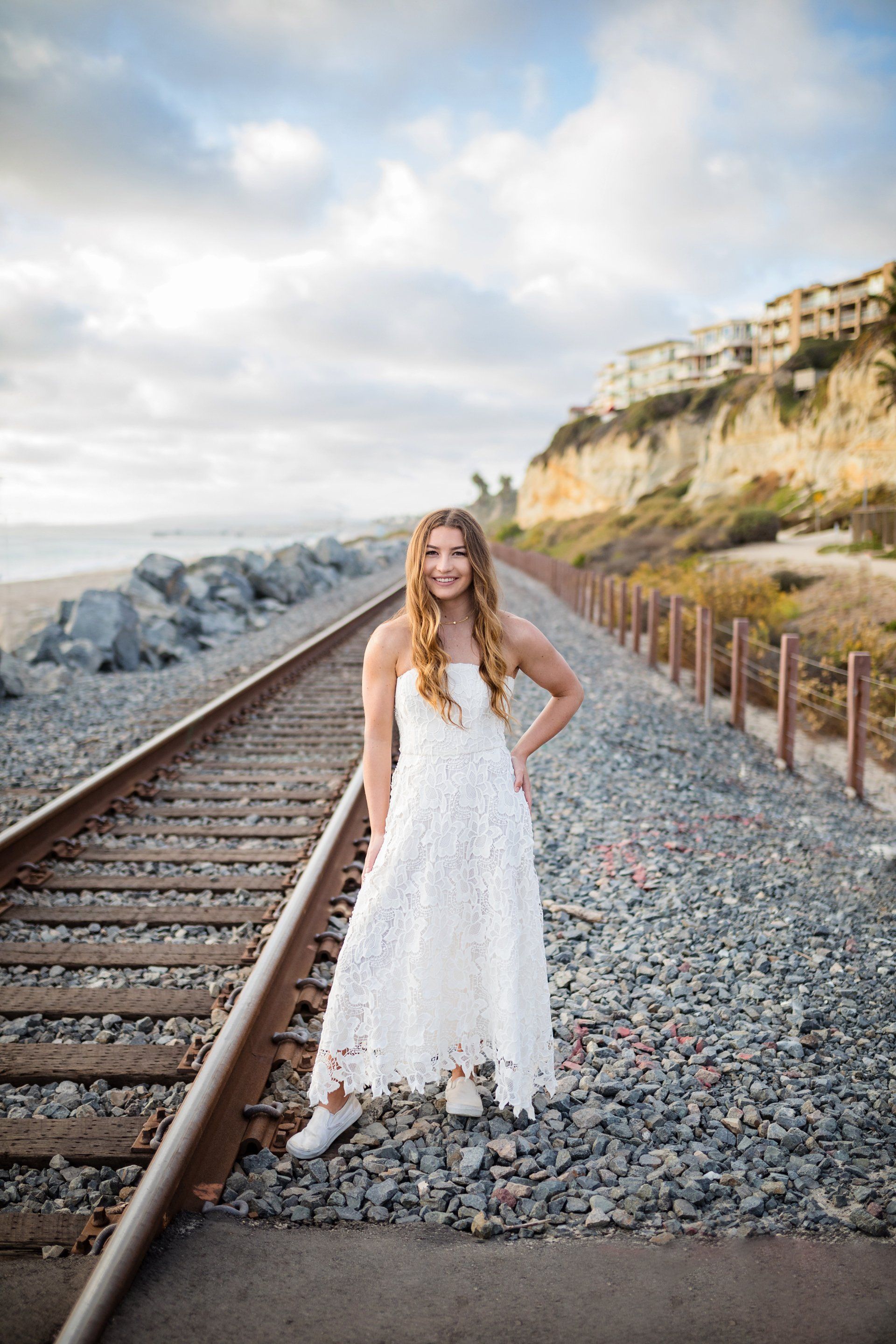 A woman in a white dress is standing on train tracks.