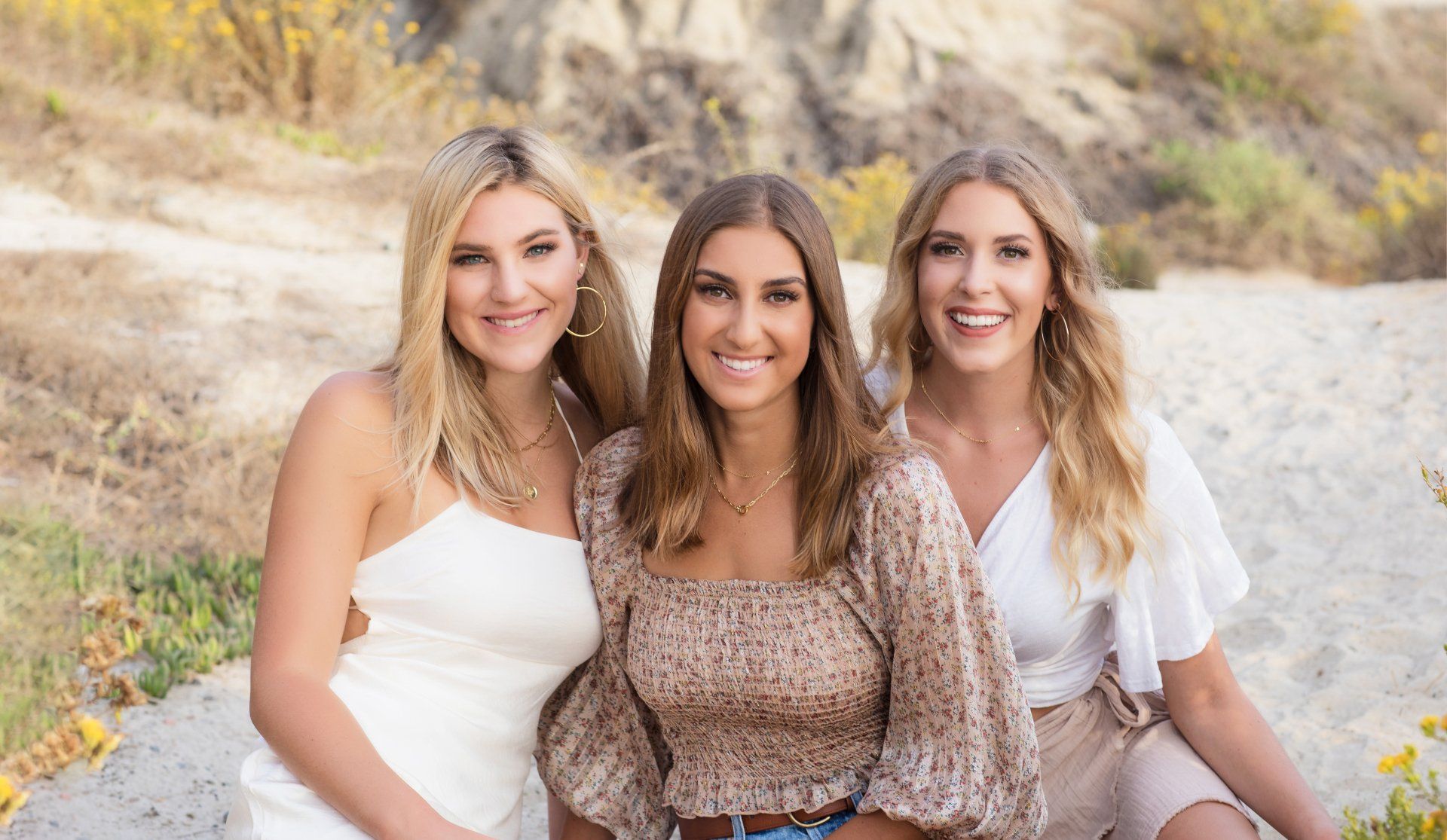 Three women are posing for a picture together while sitting on the ground.