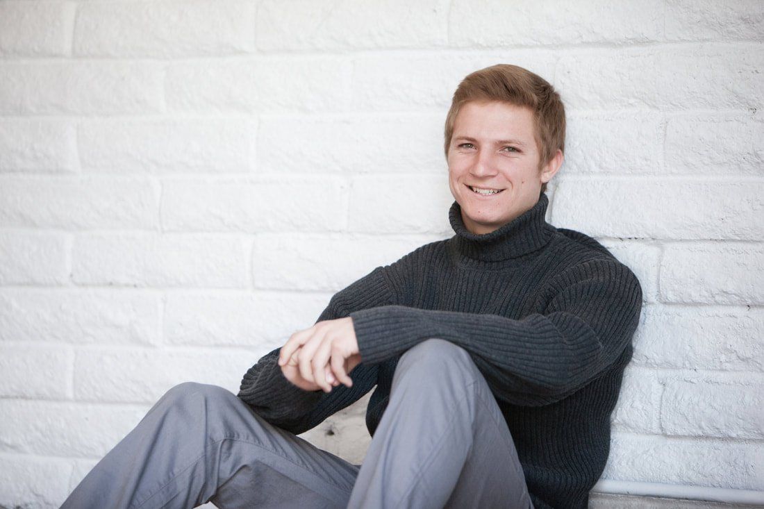 A man in a turtleneck sweater is sitting in front of a white brick wall.