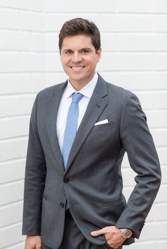 A man in a suit and tie is standing in front of a white wall.