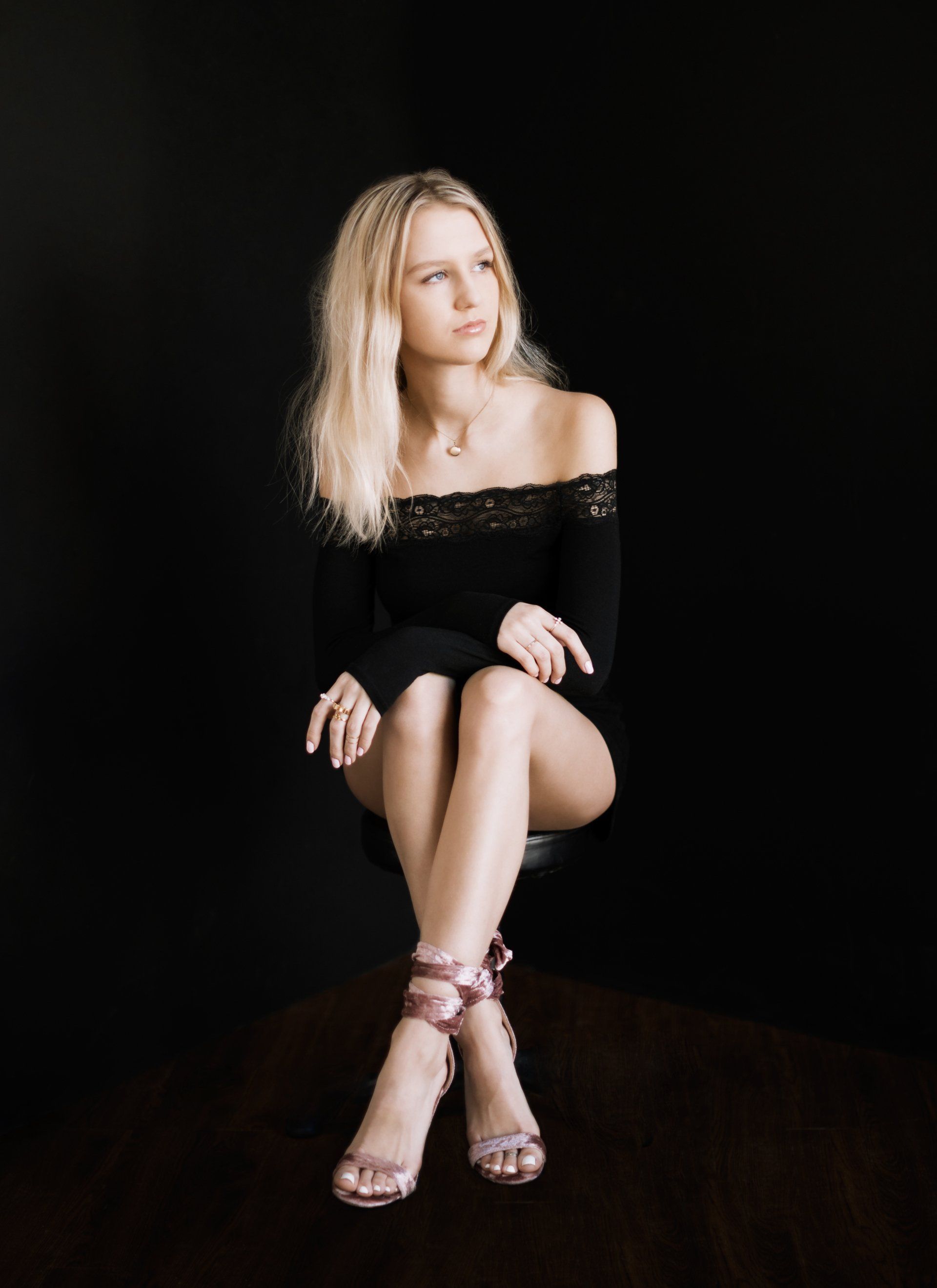 A woman in a black dress is sitting on a chair with her legs crossed.