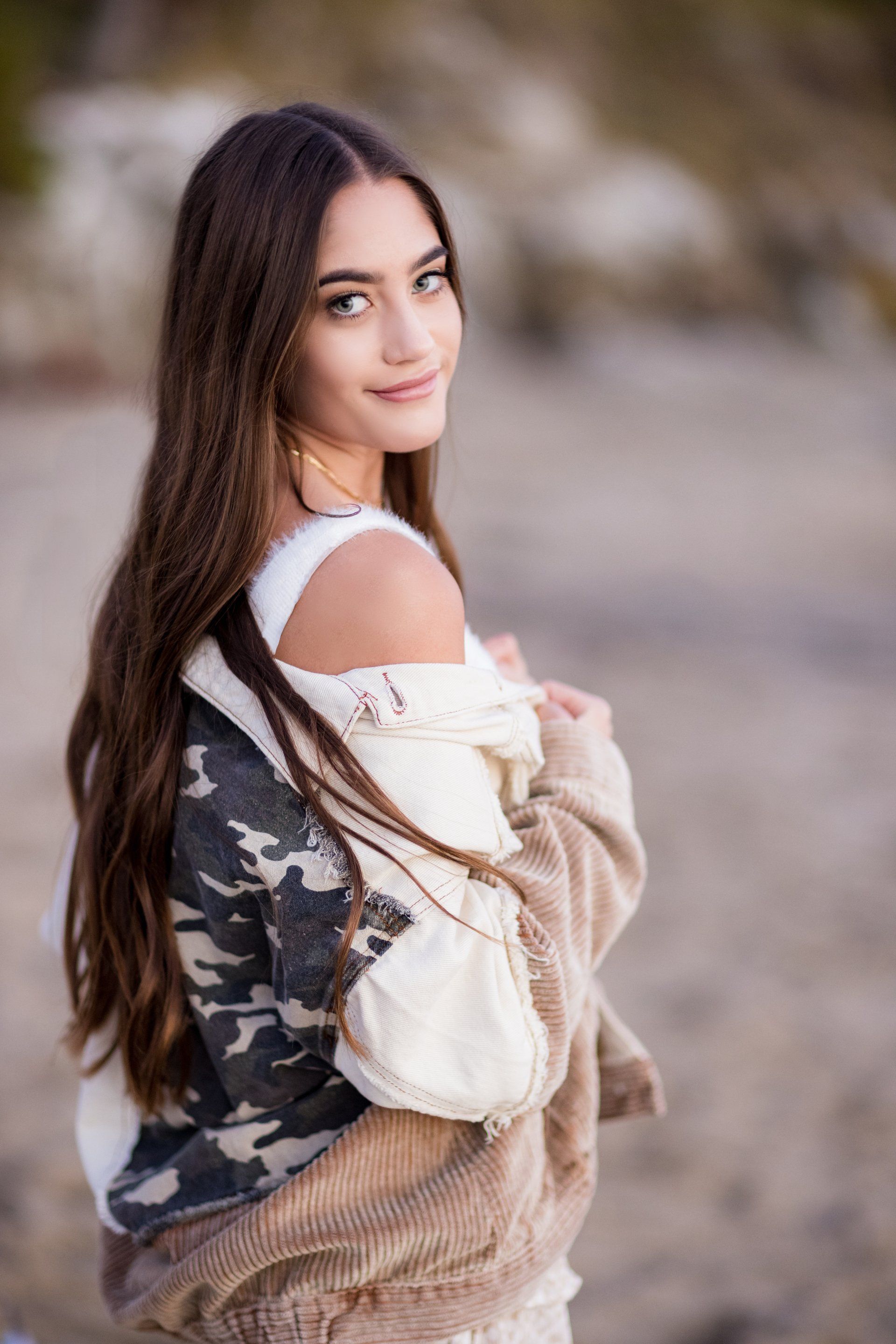 A young woman is standing on a beach wearing a camouflage jacket.